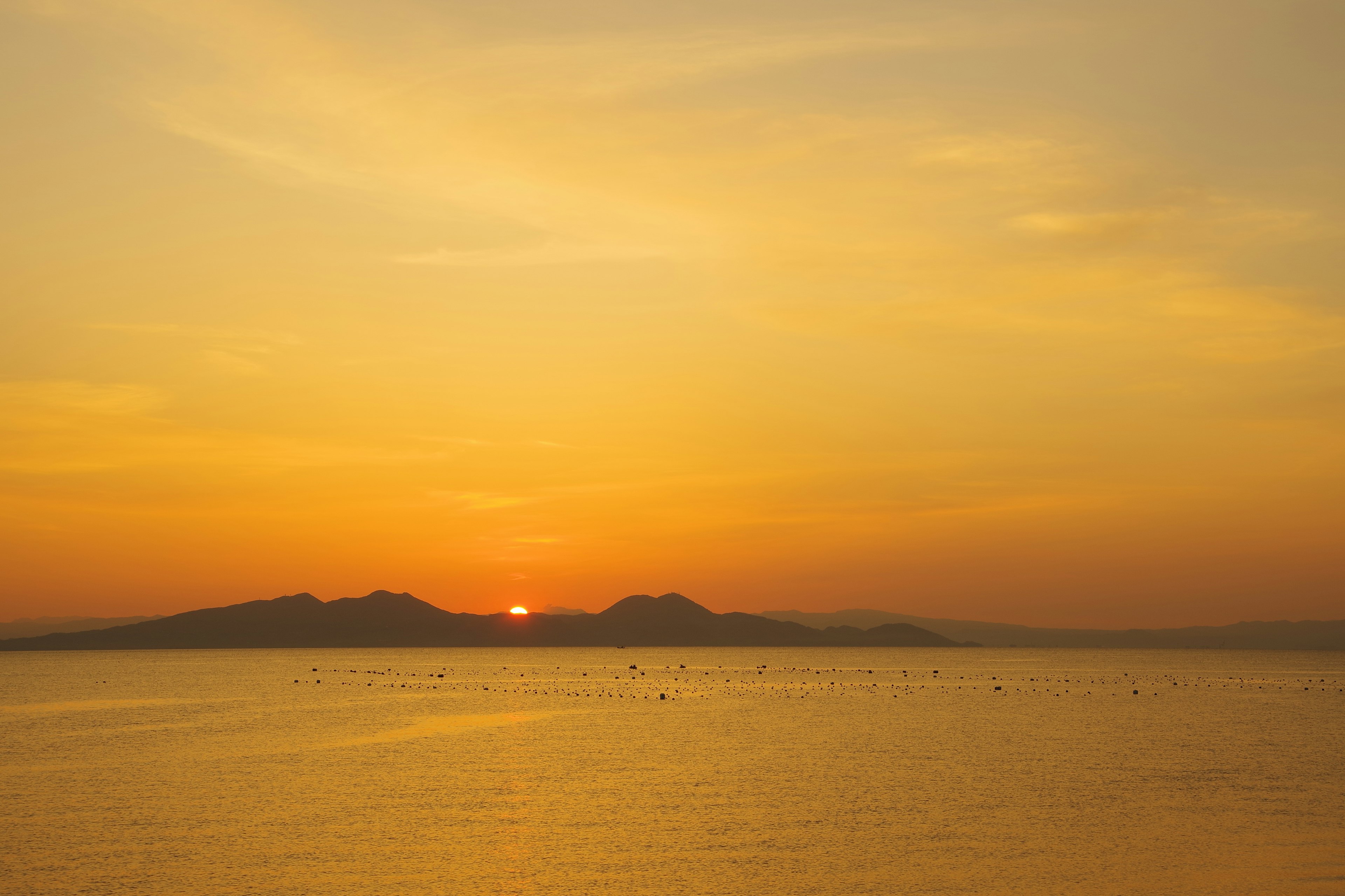 Vista escénica de la puesta de sol sobre el mar con cielo naranja y montañas