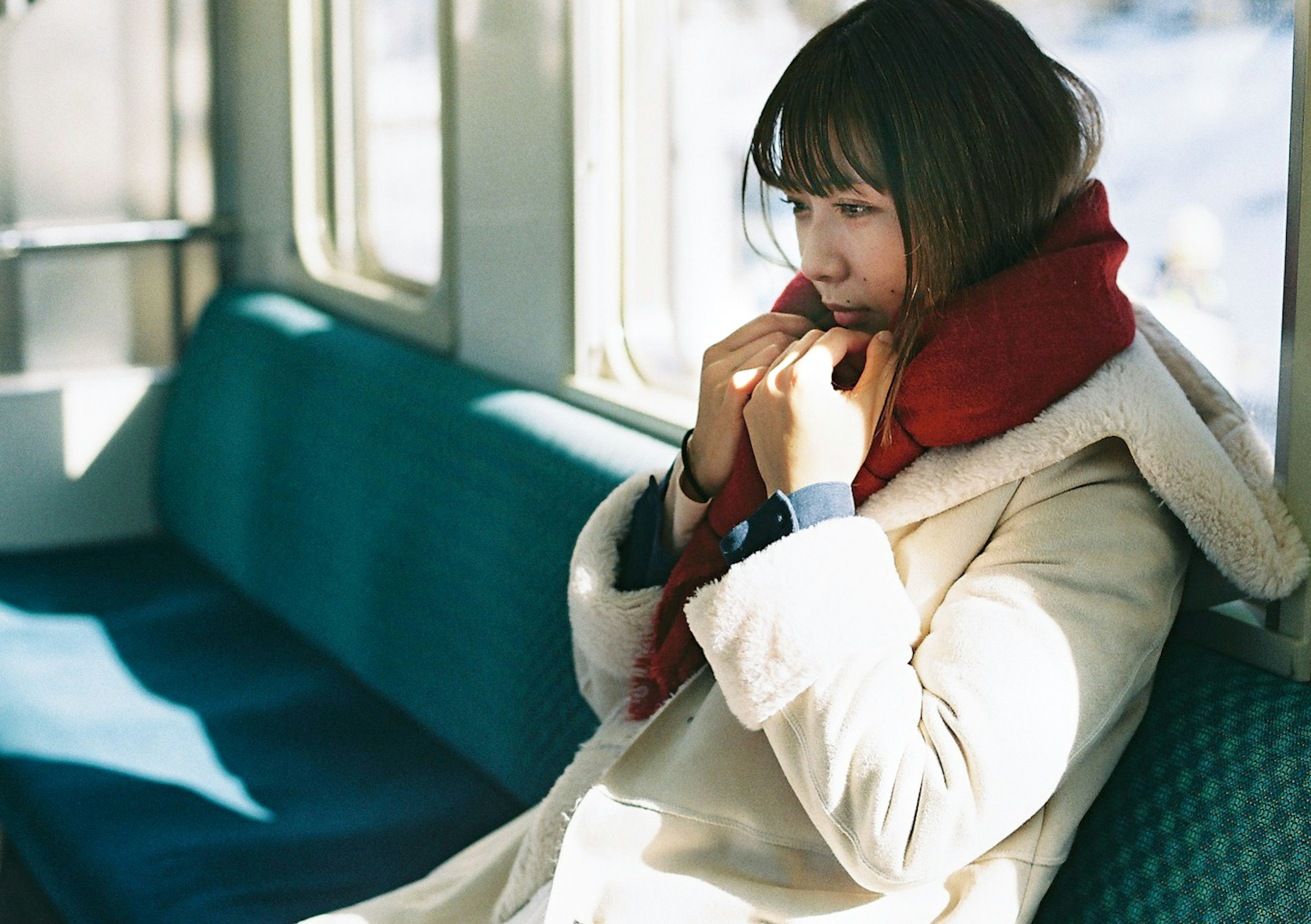 A woman sitting on a train with a red scarf wrapped around her