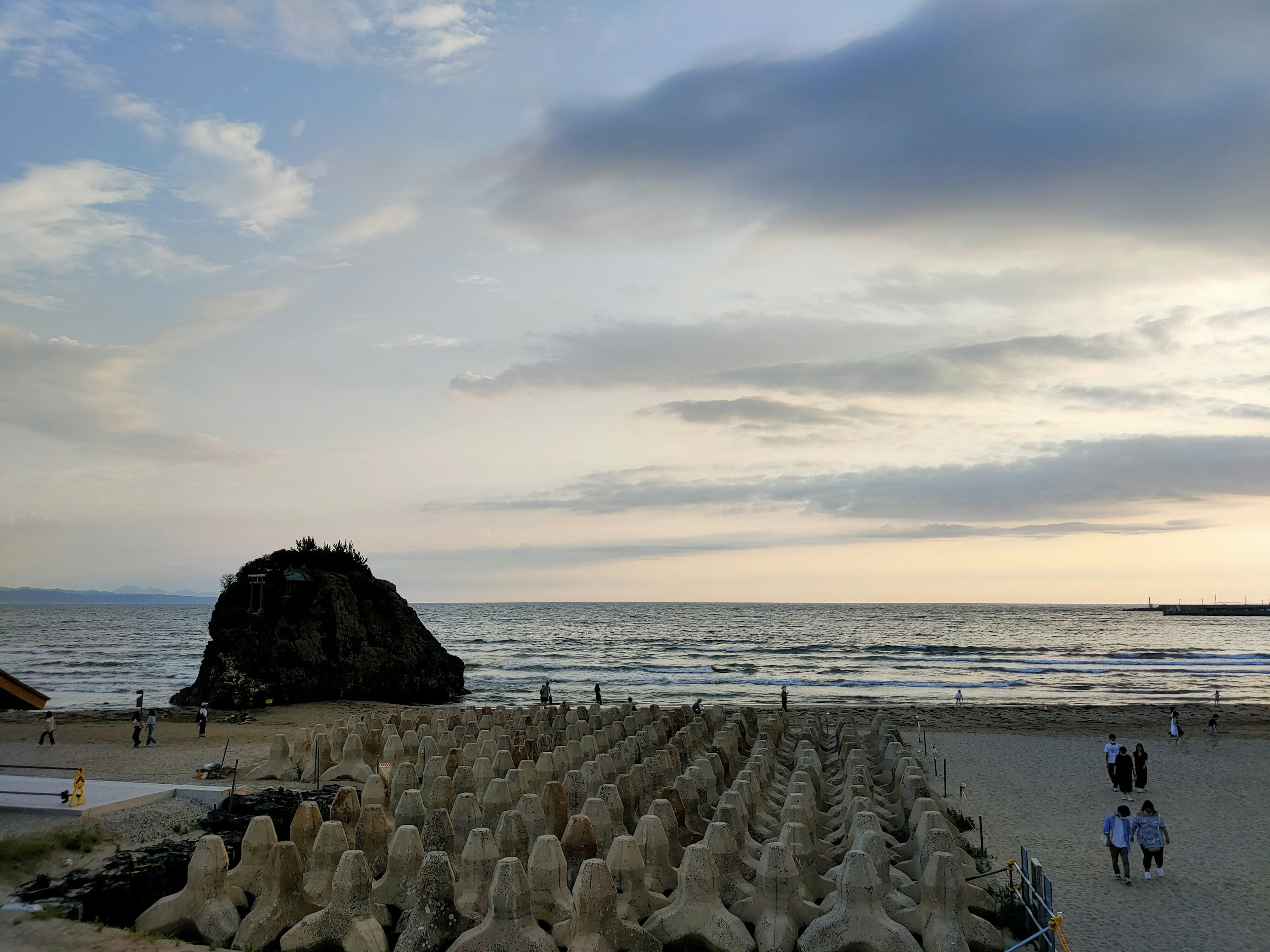 Scène de plage avec des sculptures en pierre alignées et une colline rocheuse au loin au coucher du soleil