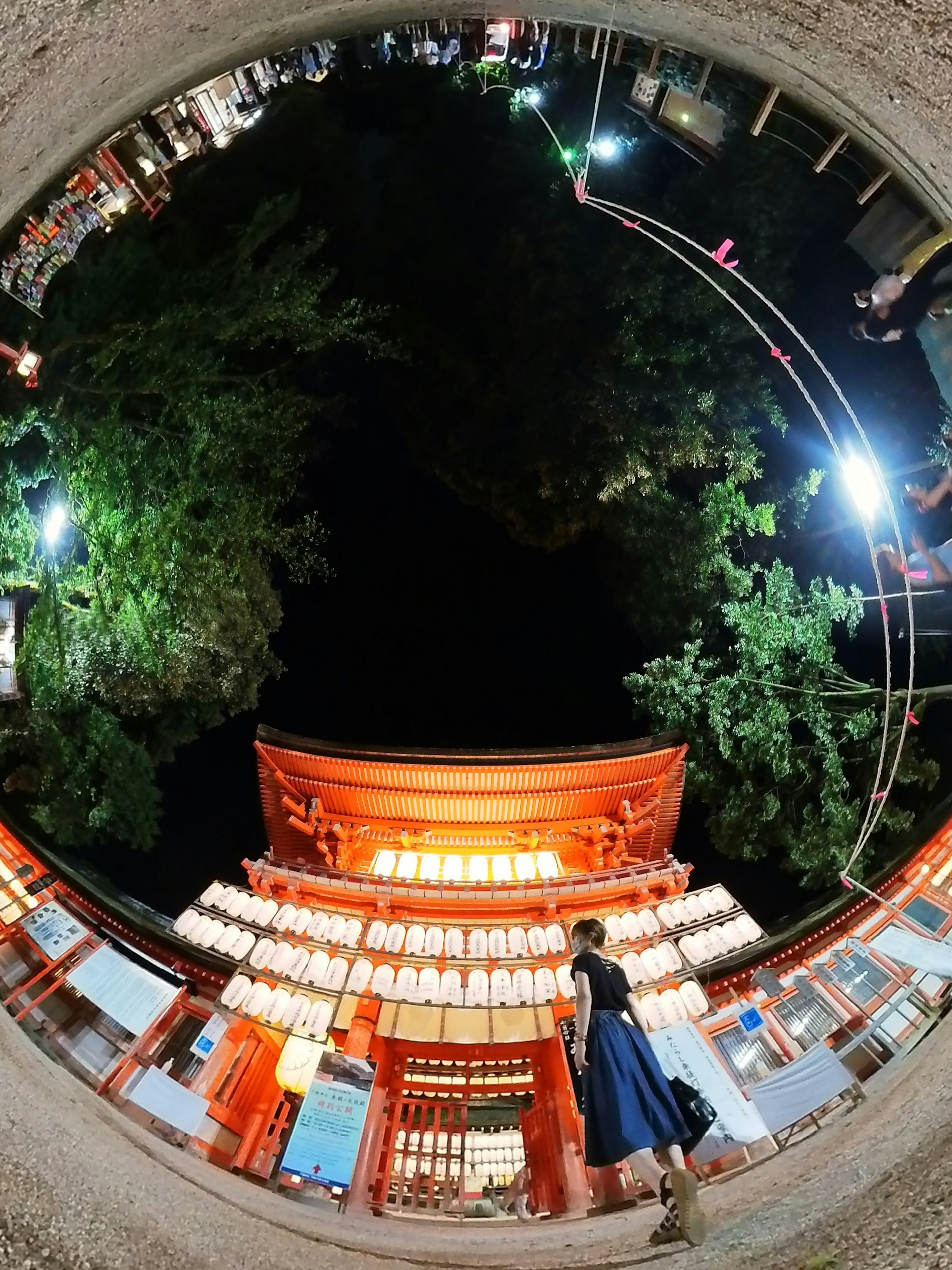 夜の神社の入り口に立つ女性 赤い鳥居と提灯が照らされている