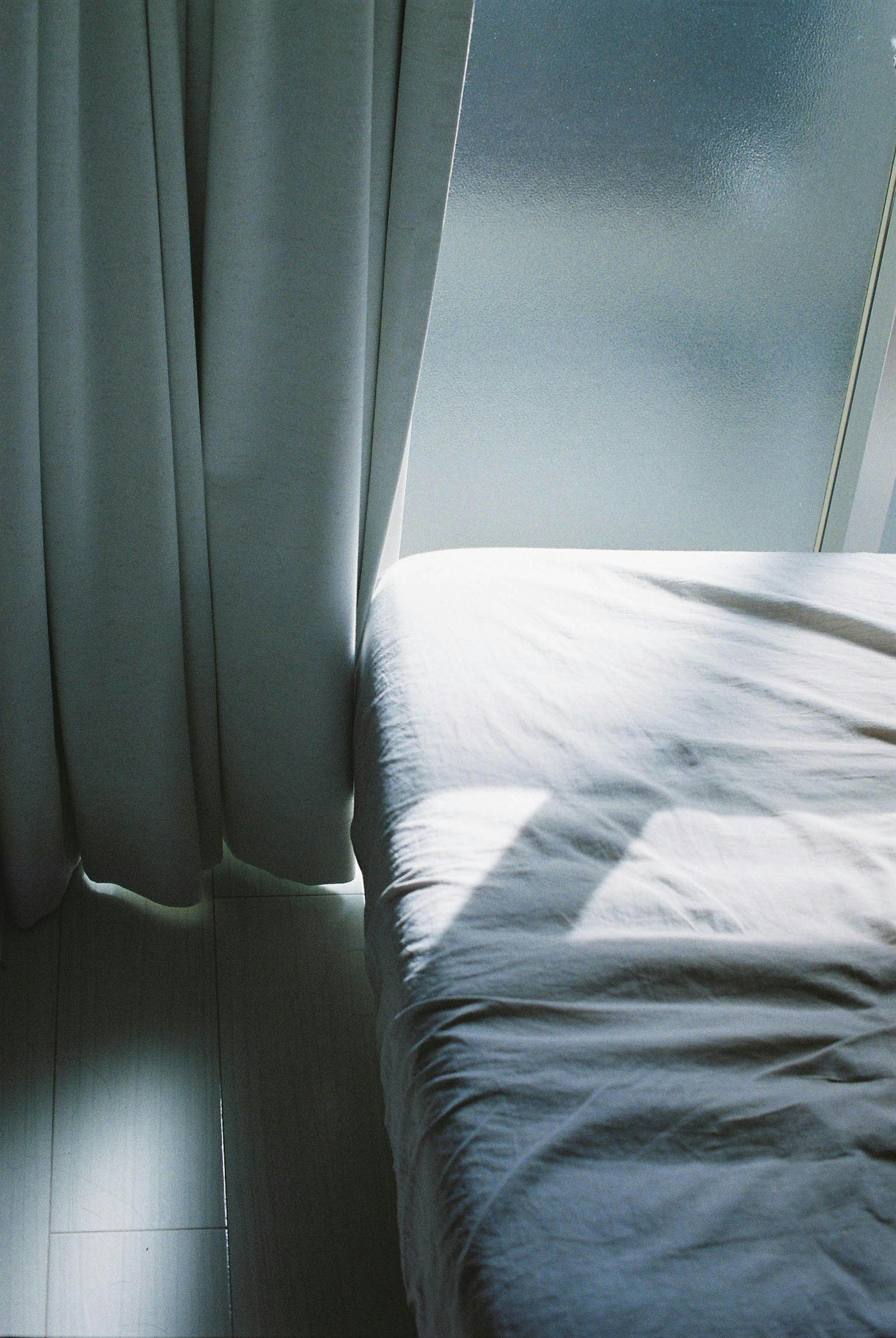 A quiet room featuring soft light on a white curtain and part of a bed