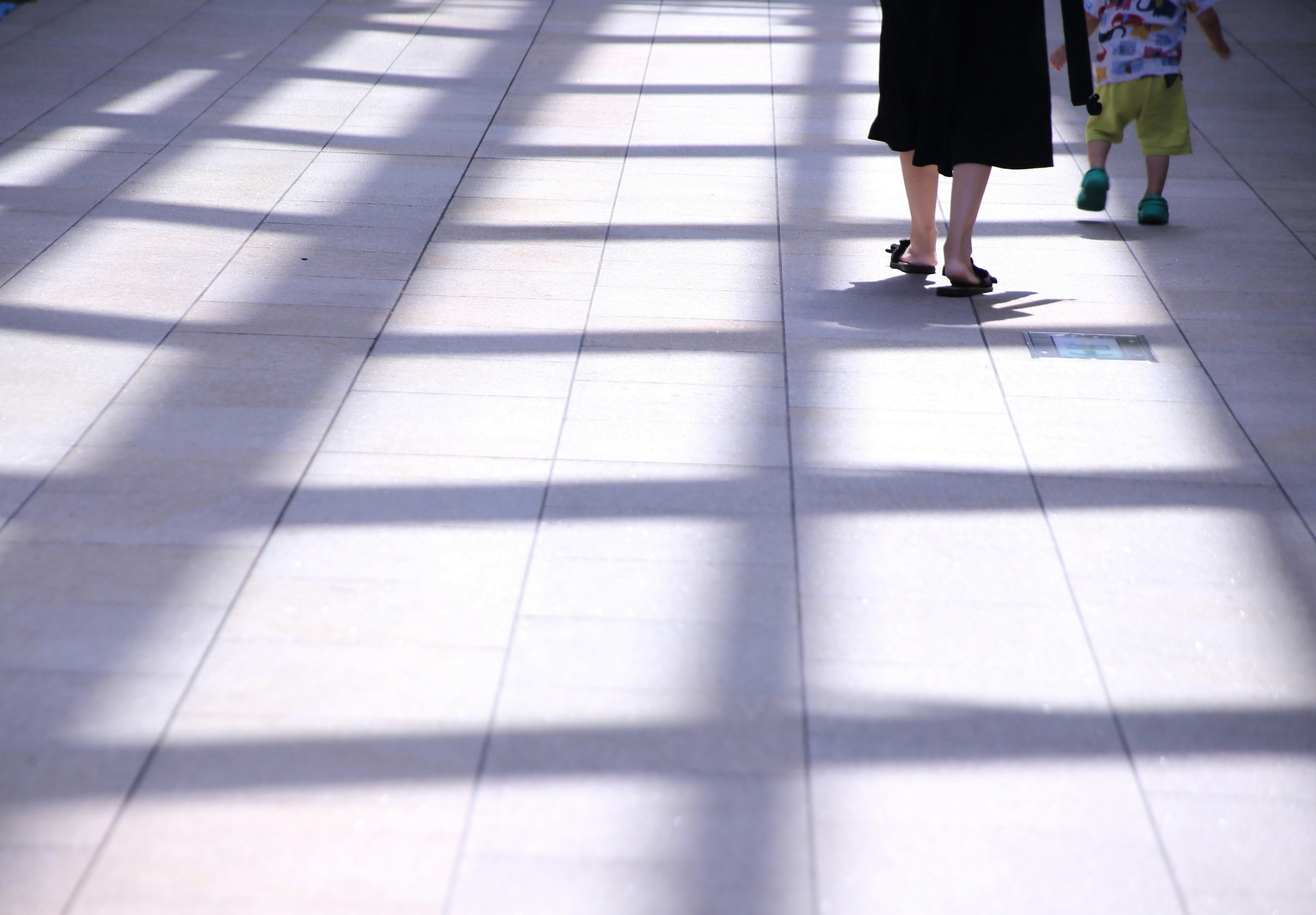 Feet of a person and a child walking on a floor with shadows