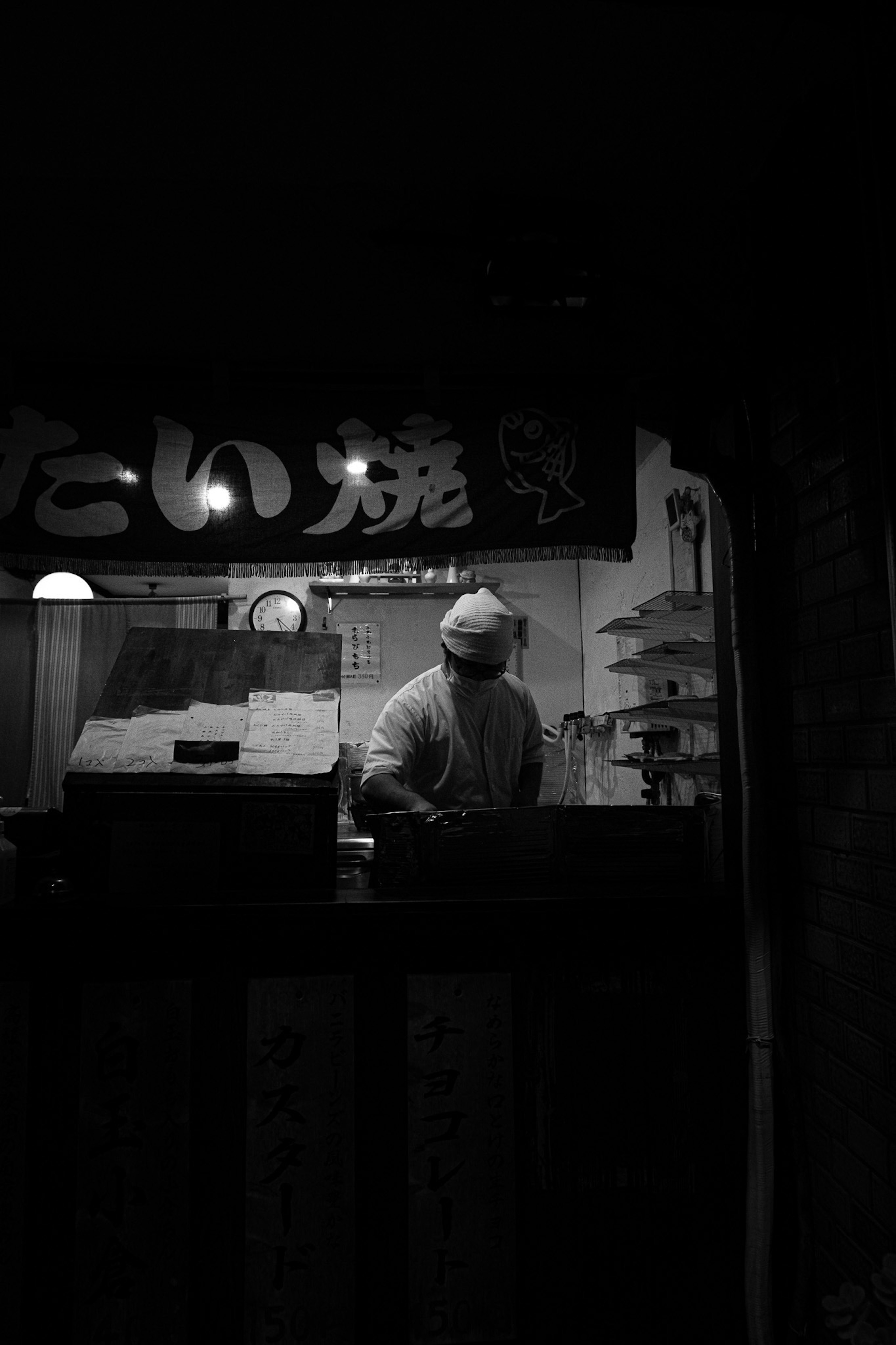 Foto en blanco y negro de un chef trabajando en un puesto con poca luz