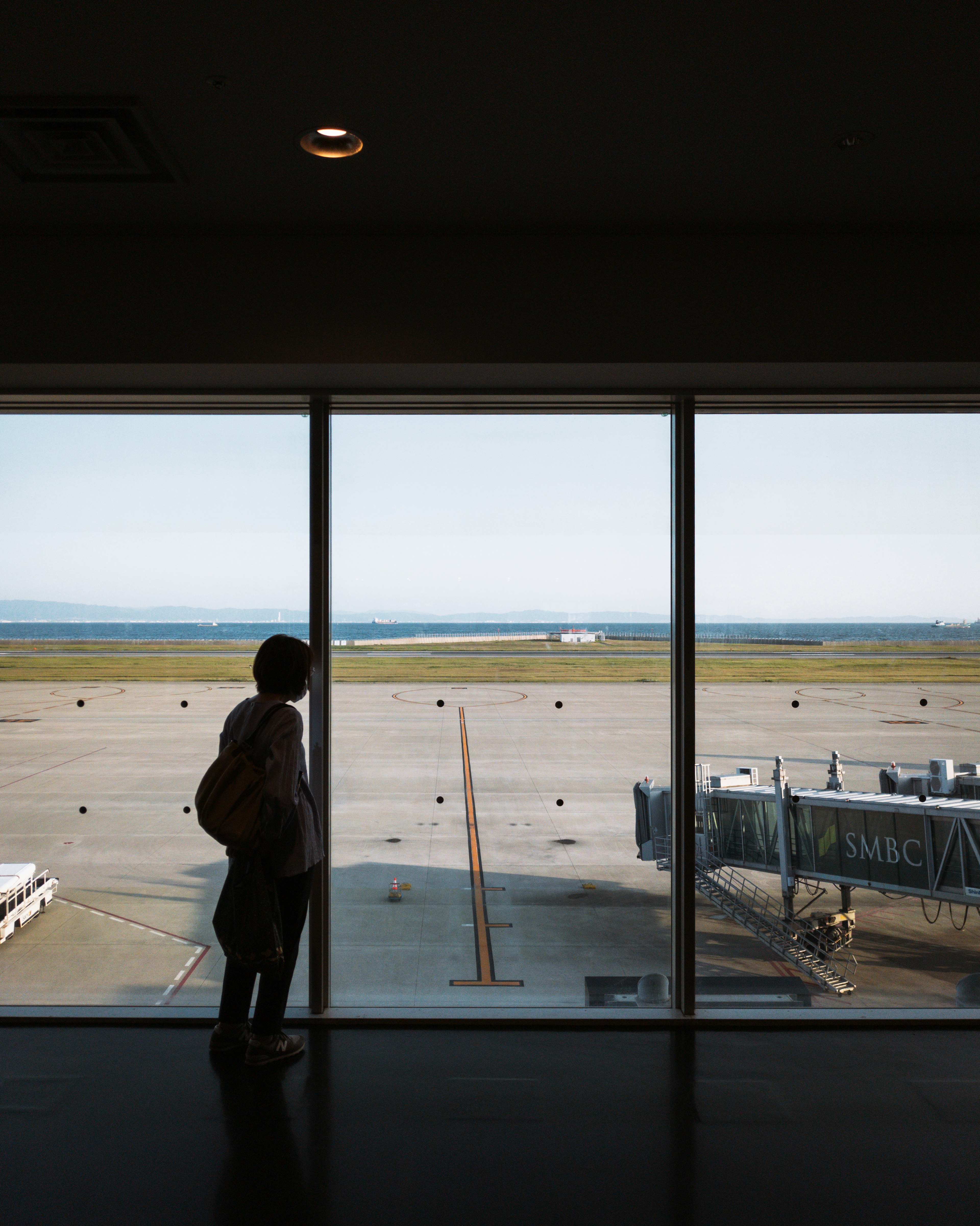 Person standing by airport window with runway view