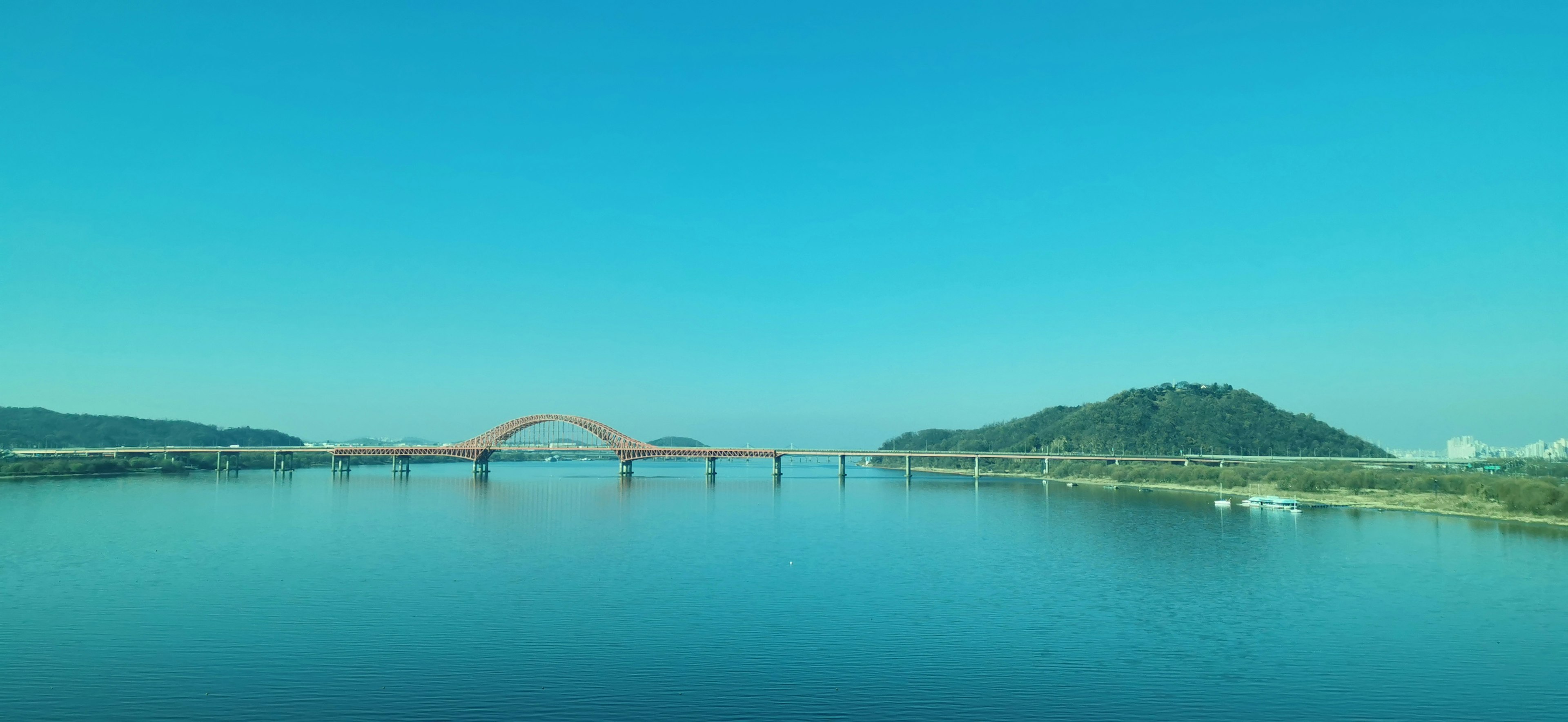 Landschaftsansicht einer Brücke über ruhigem Wasser mit einem Berg im Hintergrund