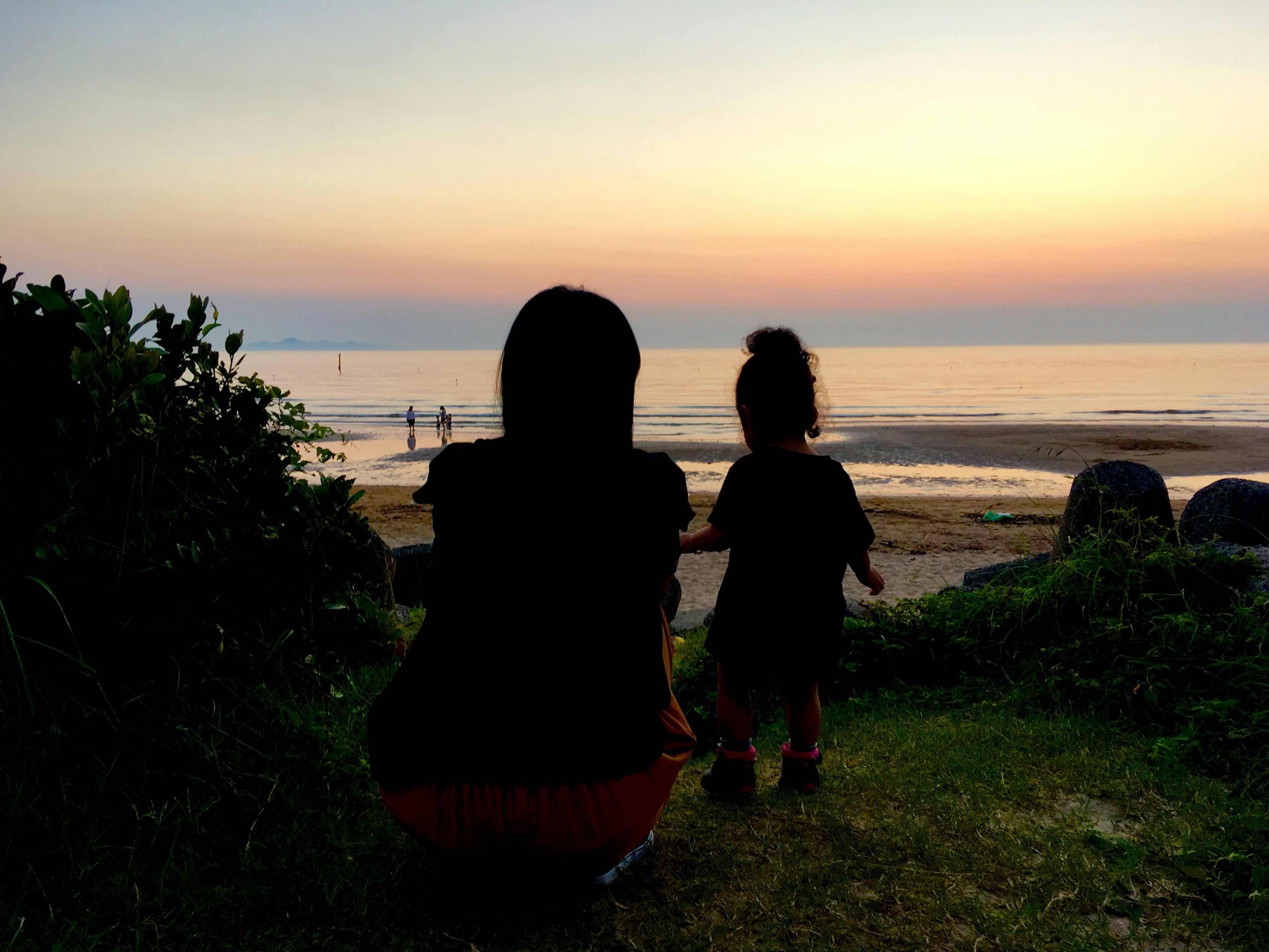 Silhouette einer Mutter und eines Kindes, die bei Sonnenuntergang auf das Meer schauen