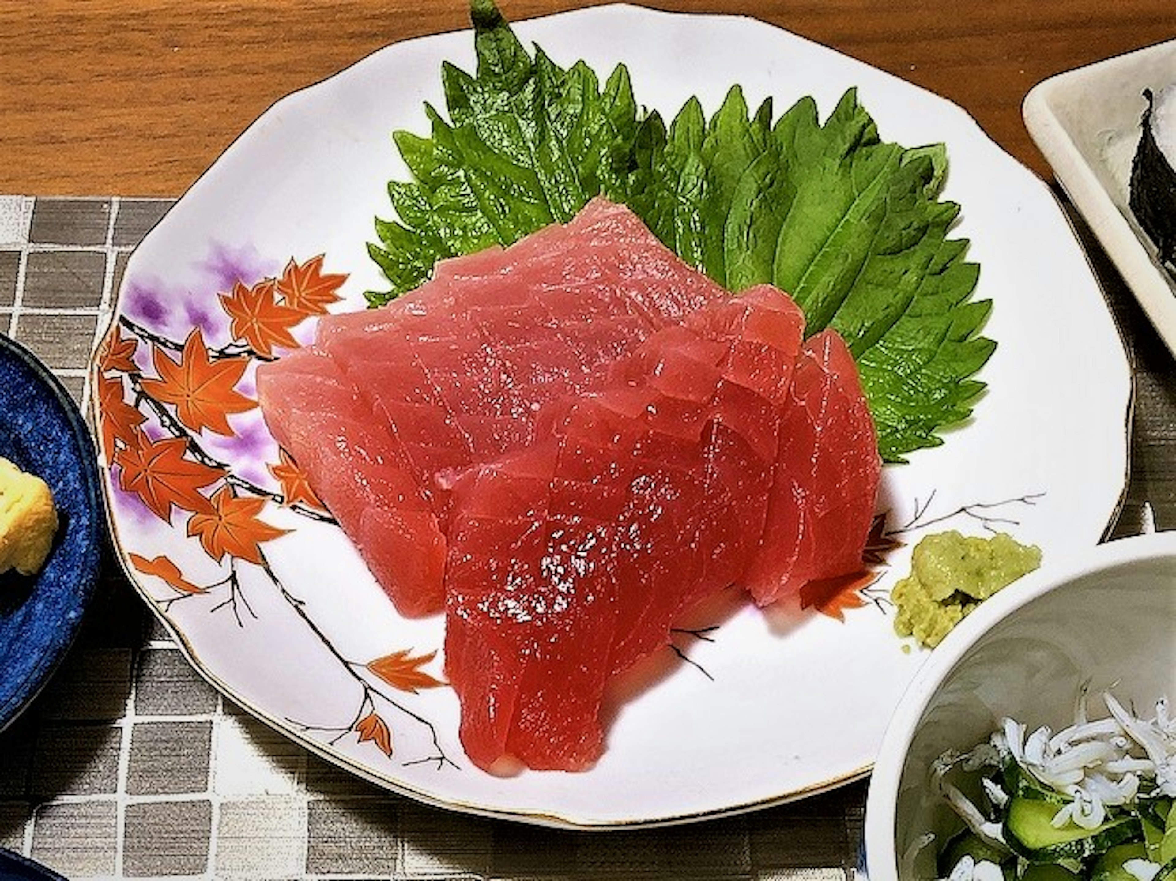 Fresh tuna sashimi arranged on a white plate with green leaves