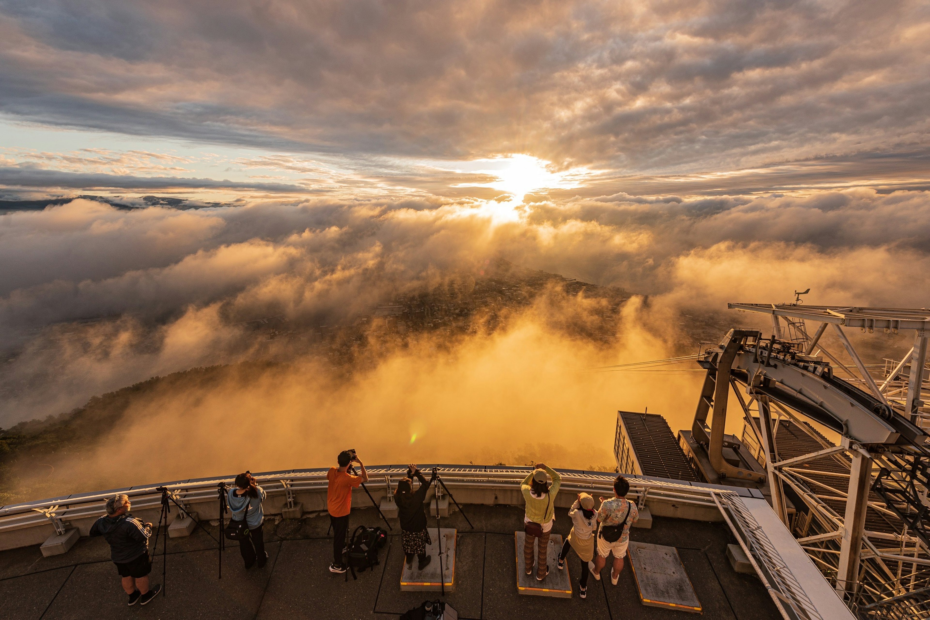 Turisti che osservano il tramonto da un punto panoramico sopra le nuvole