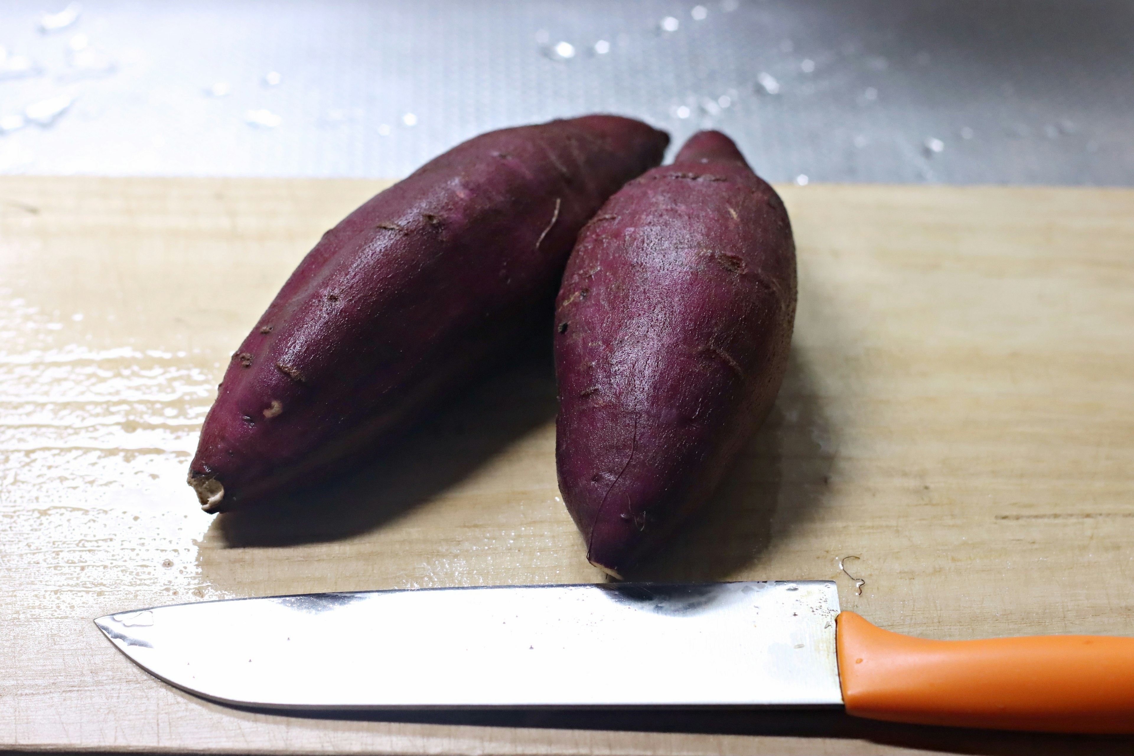 Due patate dolci viola su un tagliere di legno con un coltello arancione