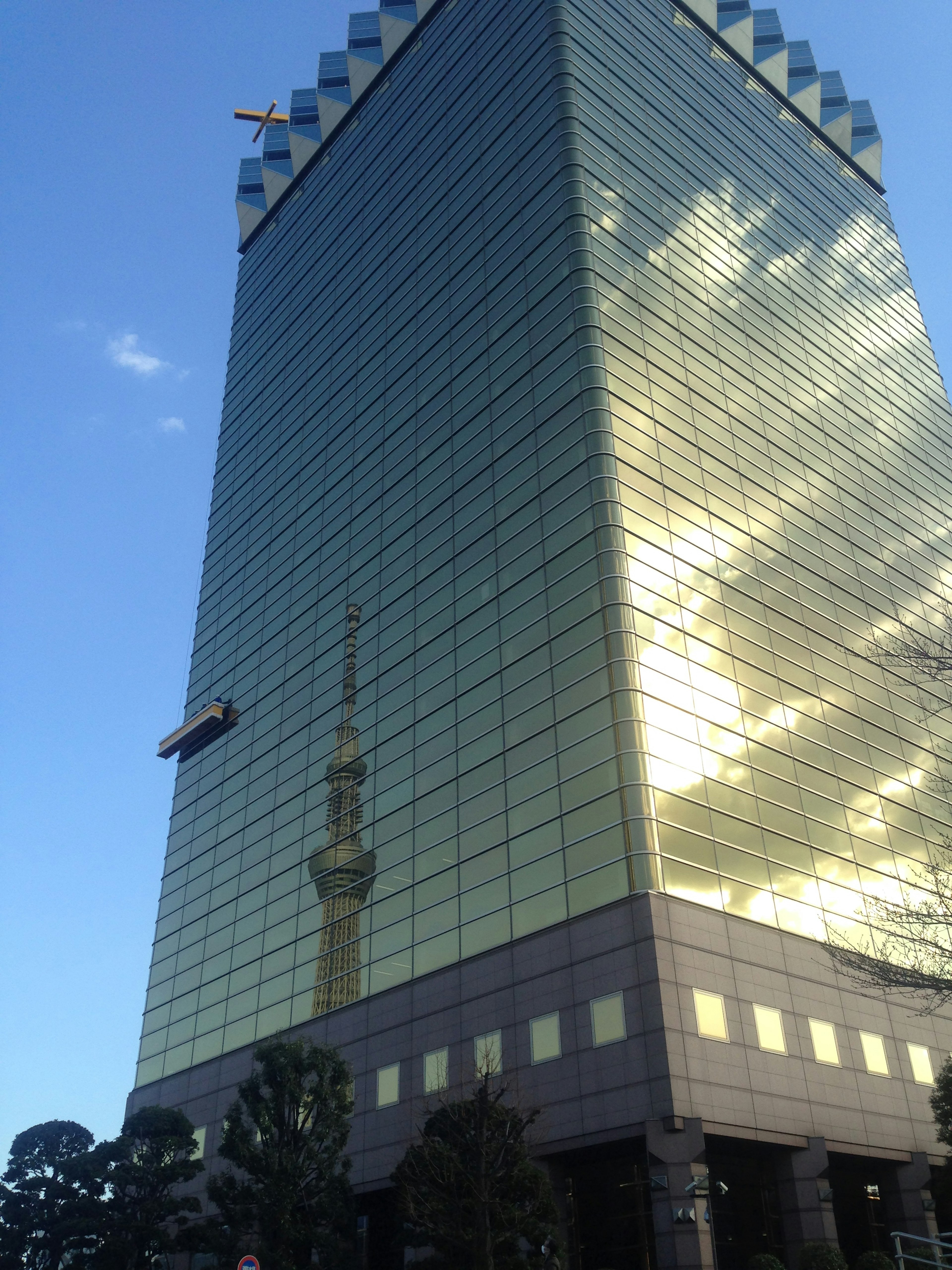 Gedung pencakar langit kaca hijau yang memantulkan Tokyo Skytree