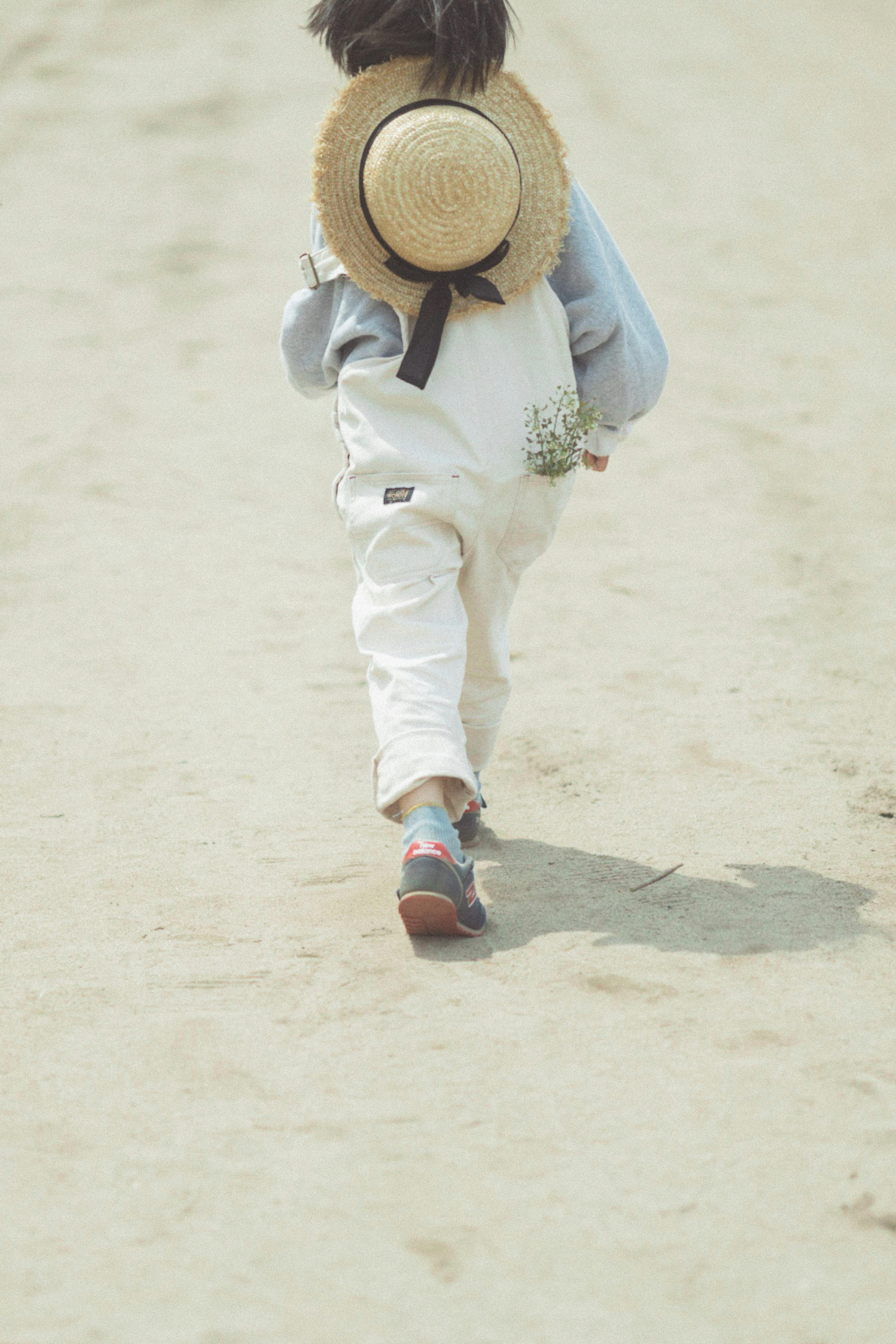 Enfant portant un chapeau de paille et une tenue blanche marchant sur un chemin de sable