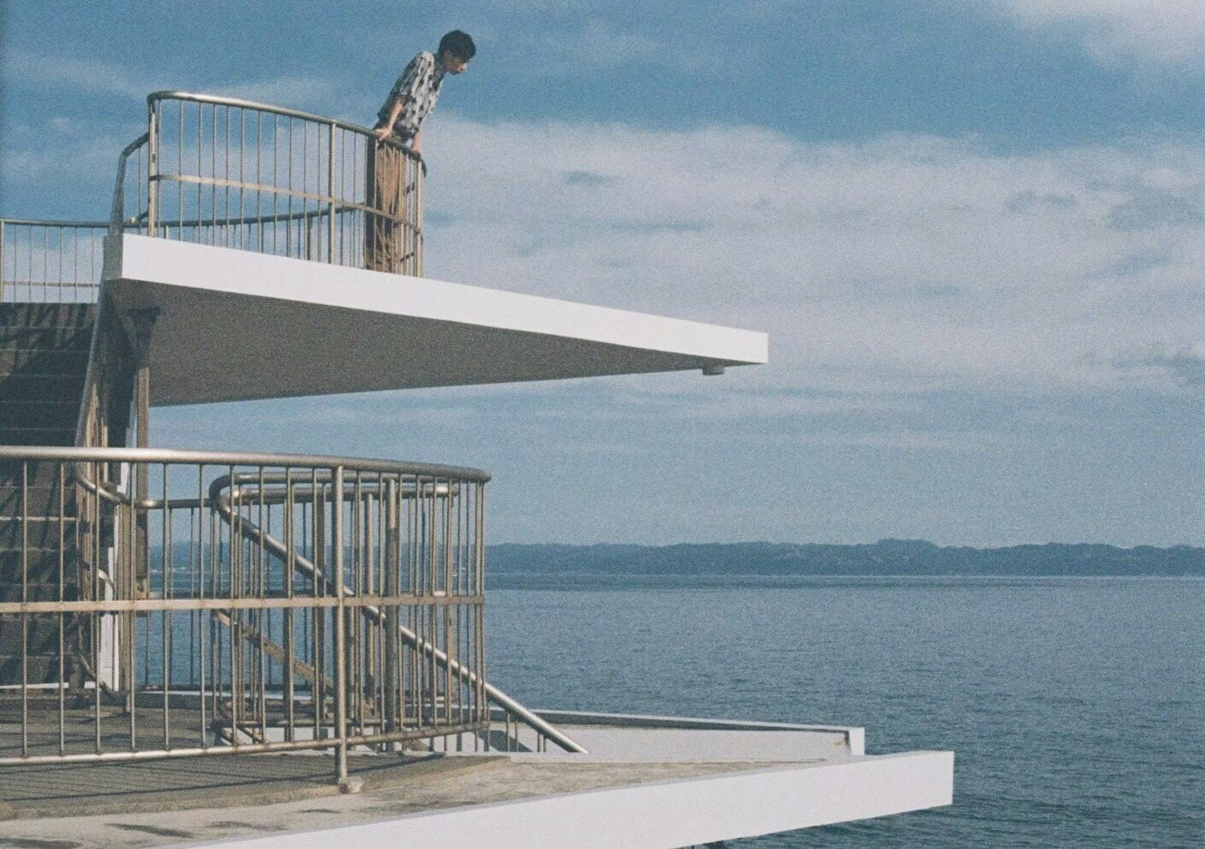 Un jeune homme en pleine réflexion sur un plongeoir blanc au-dessus de la mer