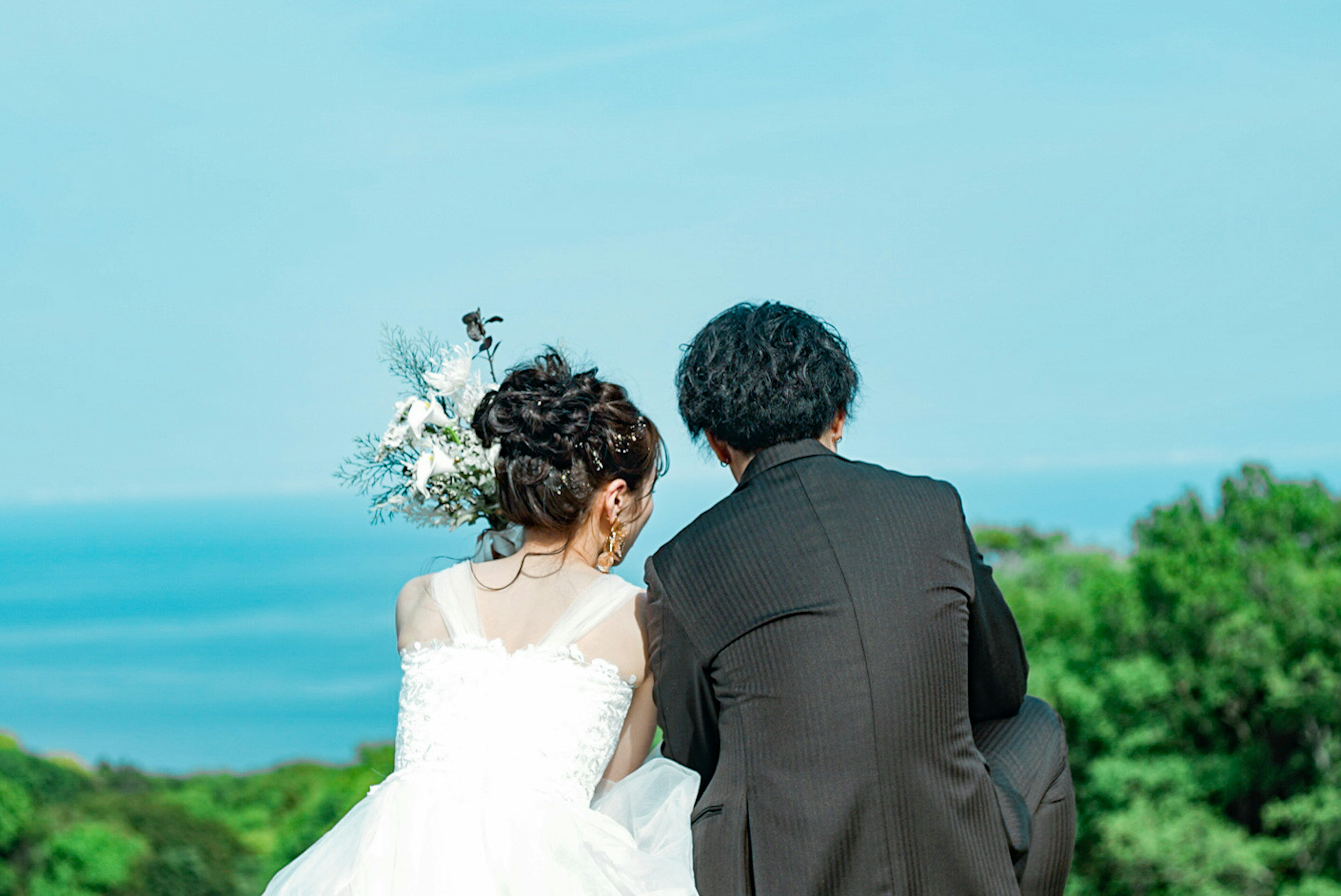 Pareja en atuendo de boda sentada juntos con vista al océano y vegetación