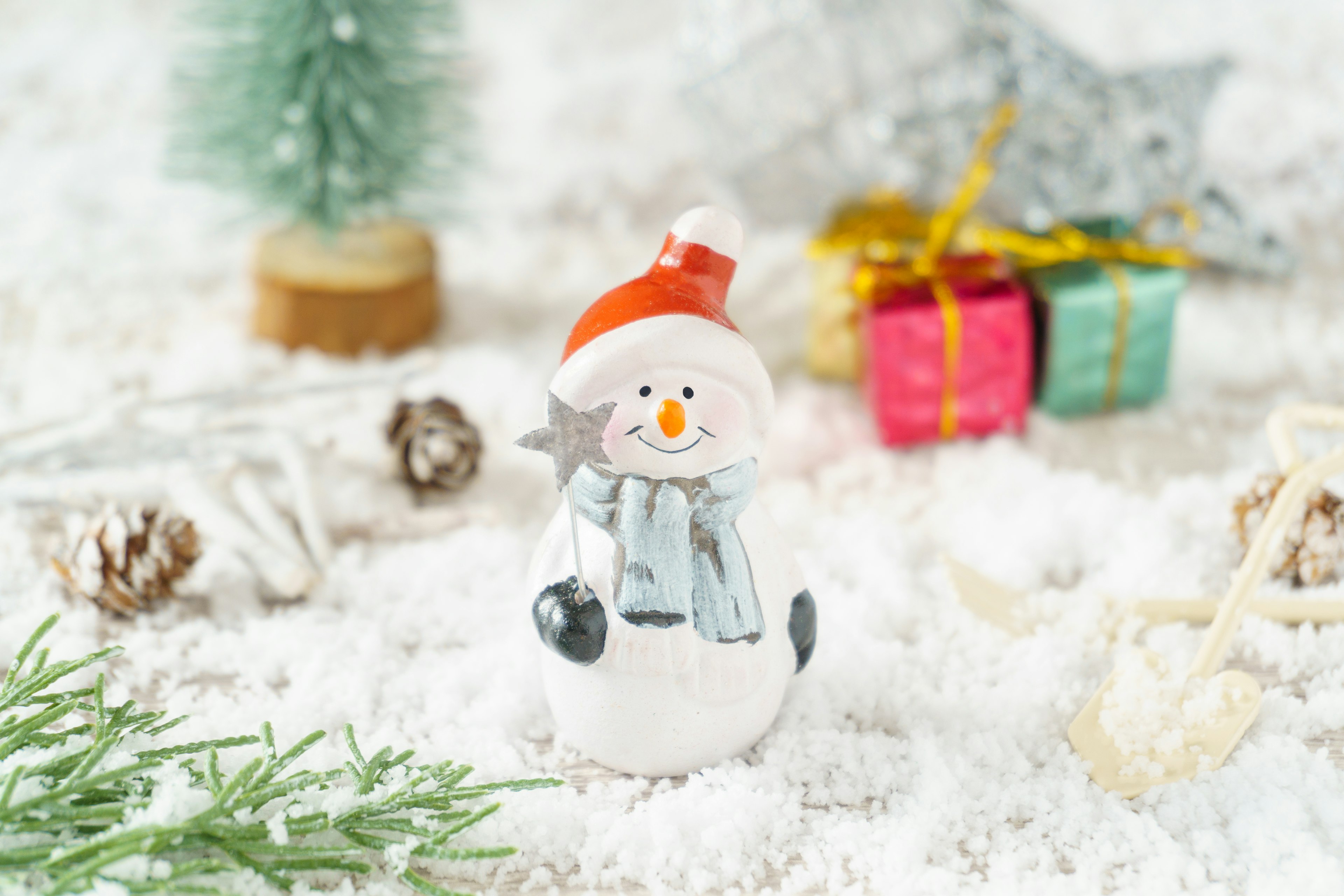 Un piccolo pupazzo di neve sulla neve con un albero di Natale e regali colorati sullo sfondo