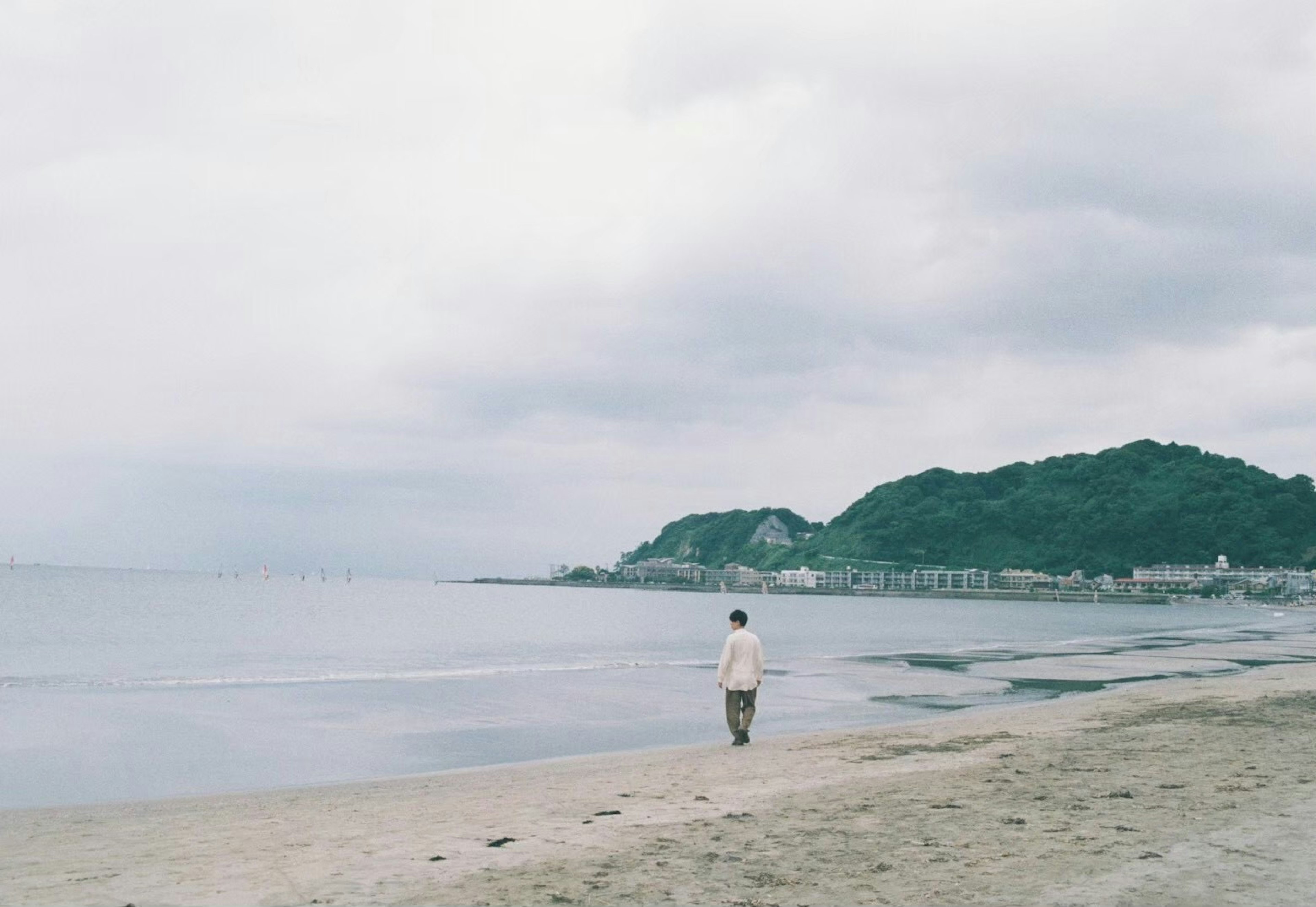 A person walking along a quiet beach under a cloudy sky