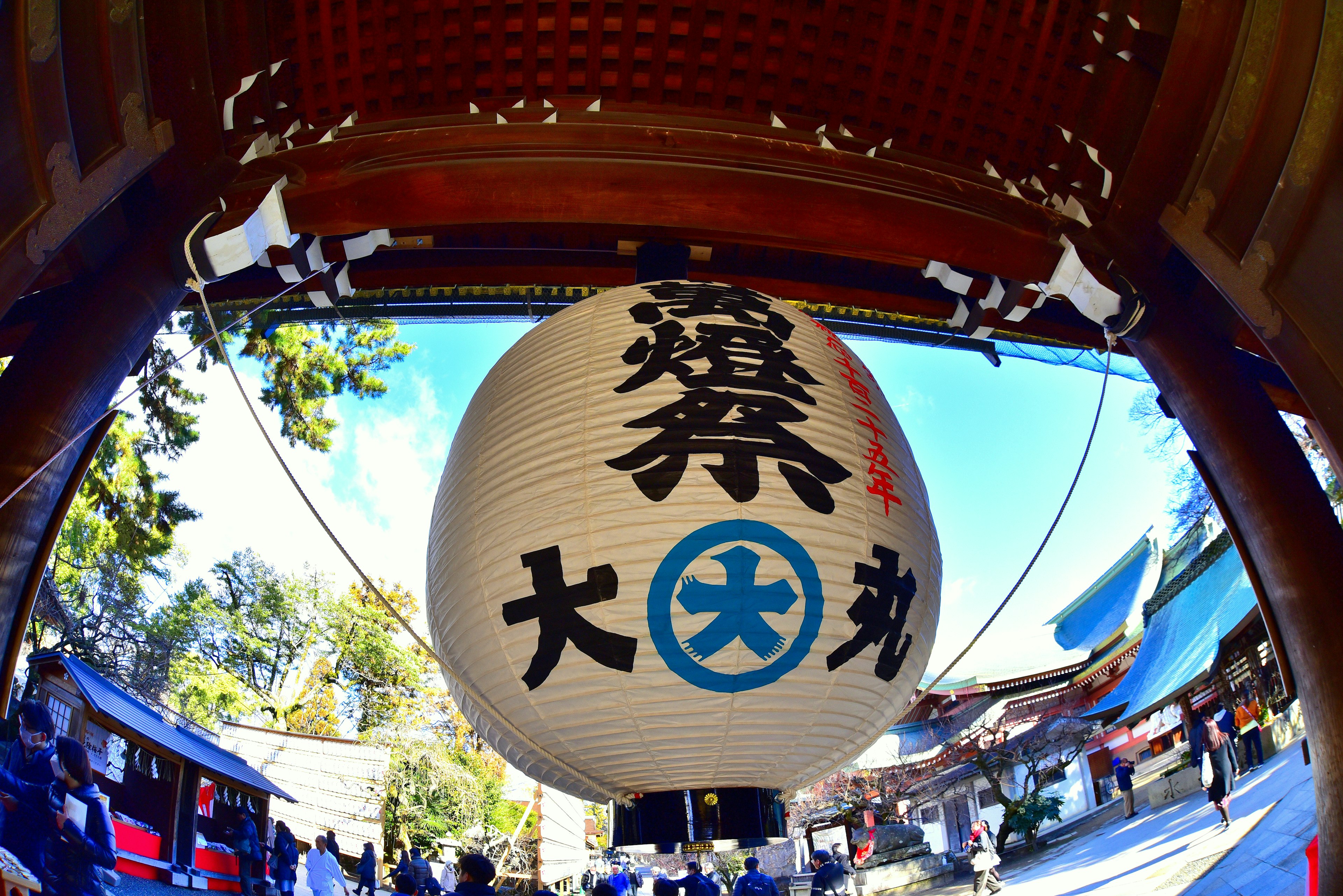 Large lantern hanging in a shrine courtyard with visitors