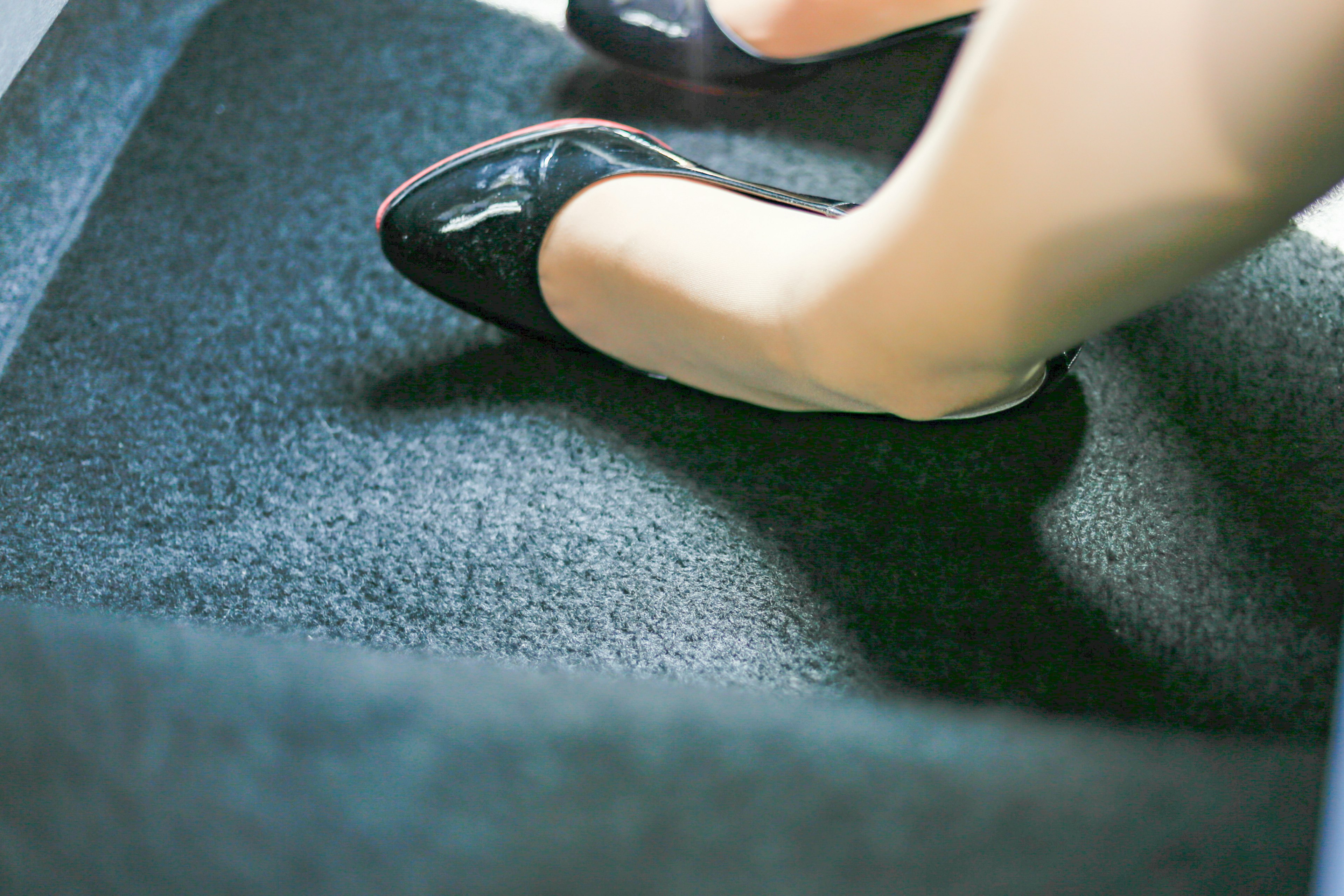 A foot in a black high heel resting on a carpet