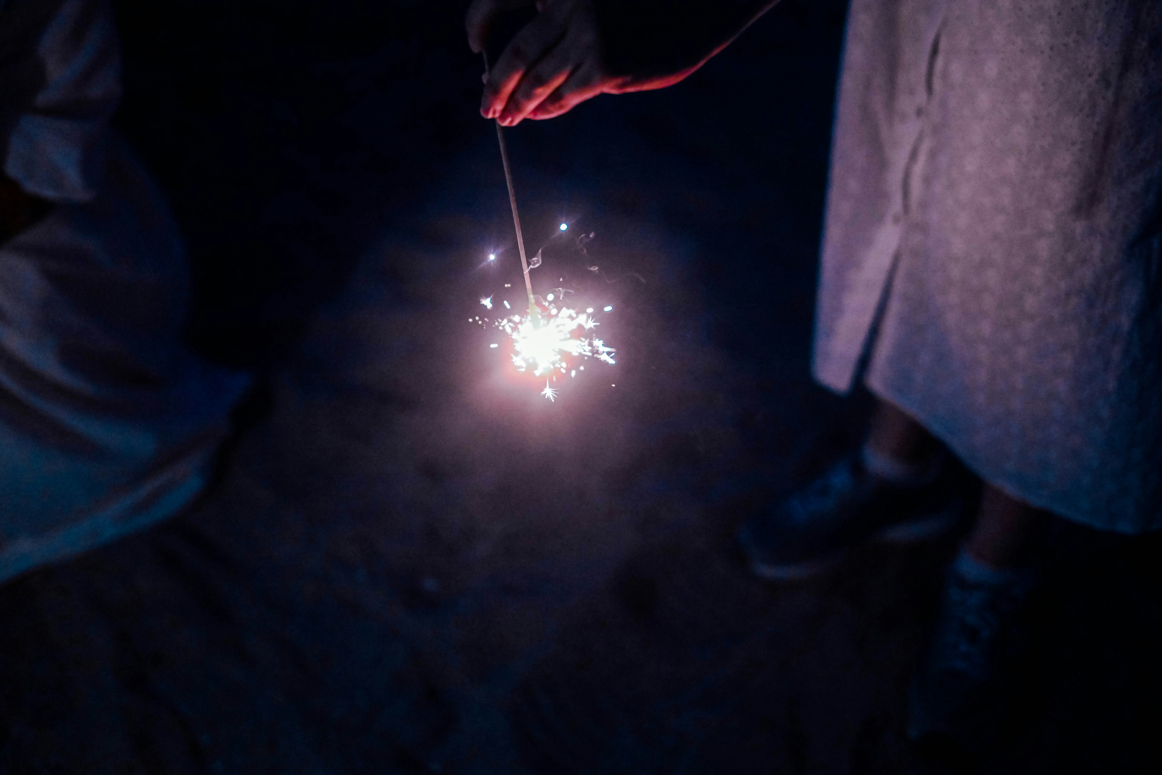 Hand holding a sparkler in the dark with glowing sparks