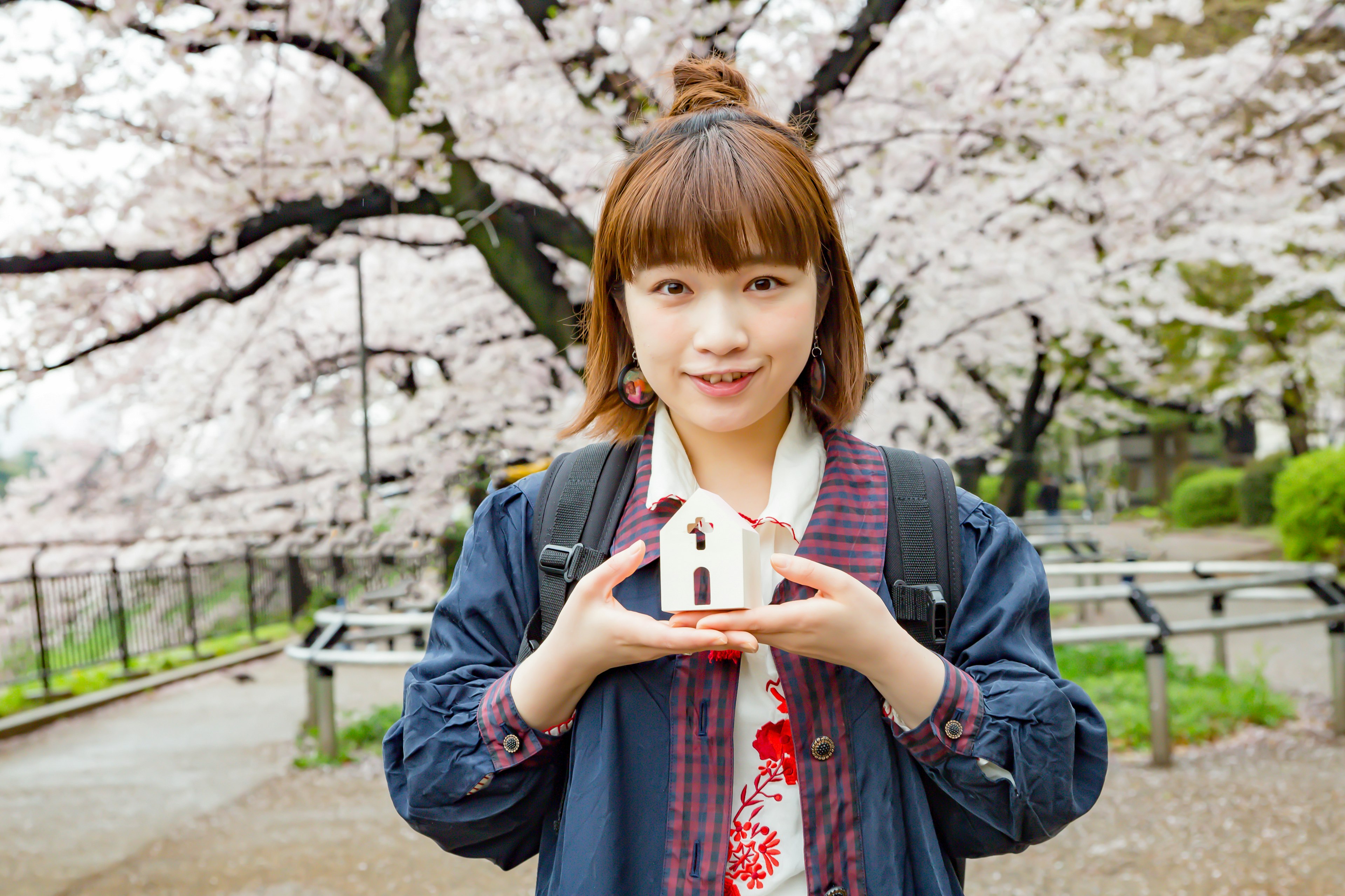 Woman holding a miniature house under cherry blossom trees