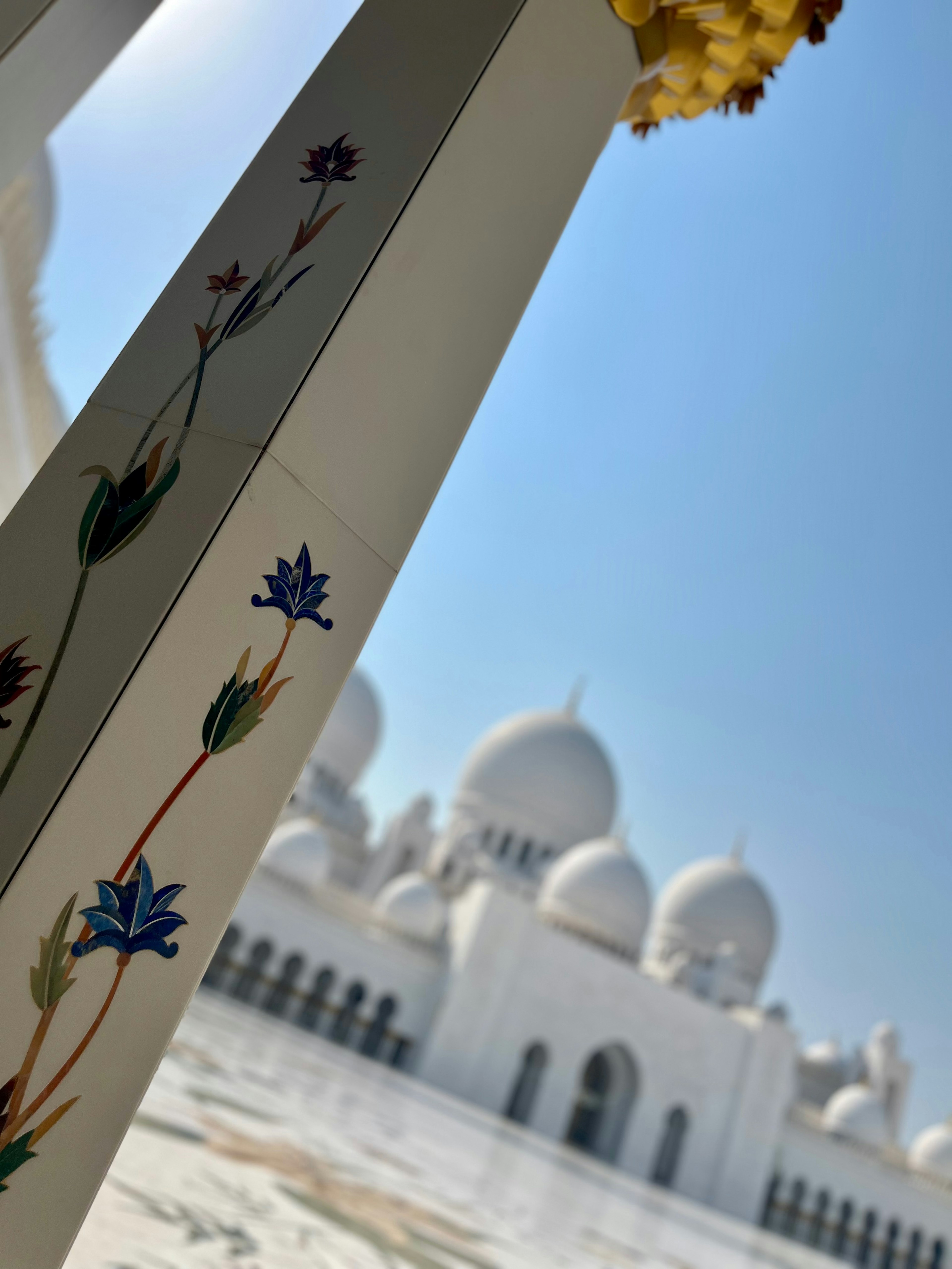 Columna con diseños florales en primer plano y cúpulas de mezquita blanca al fondo