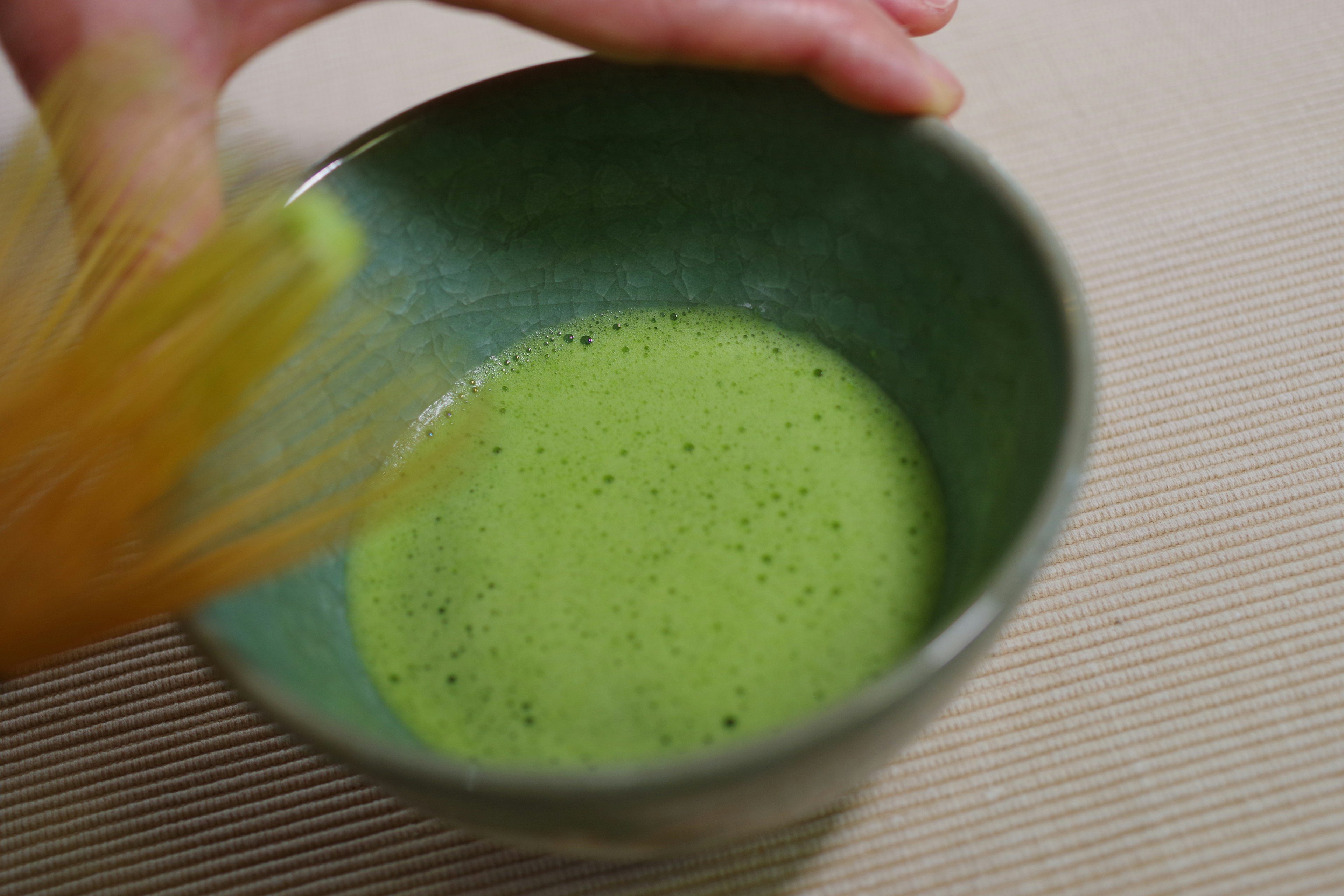 Hand whisking matcha in a green bowl