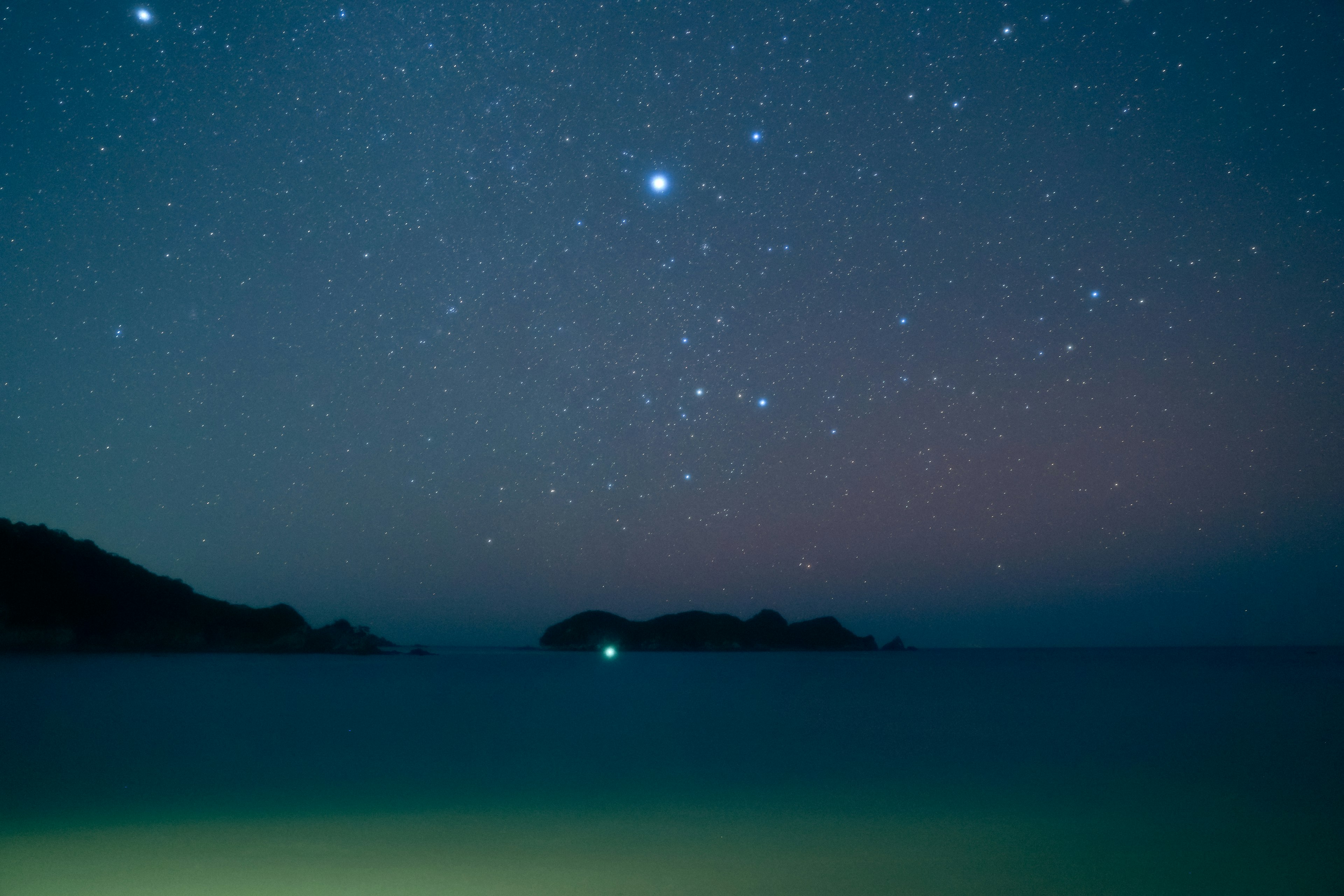 Langit malam penuh bintang di atas laut tenang dengan pulau kecil terlihat