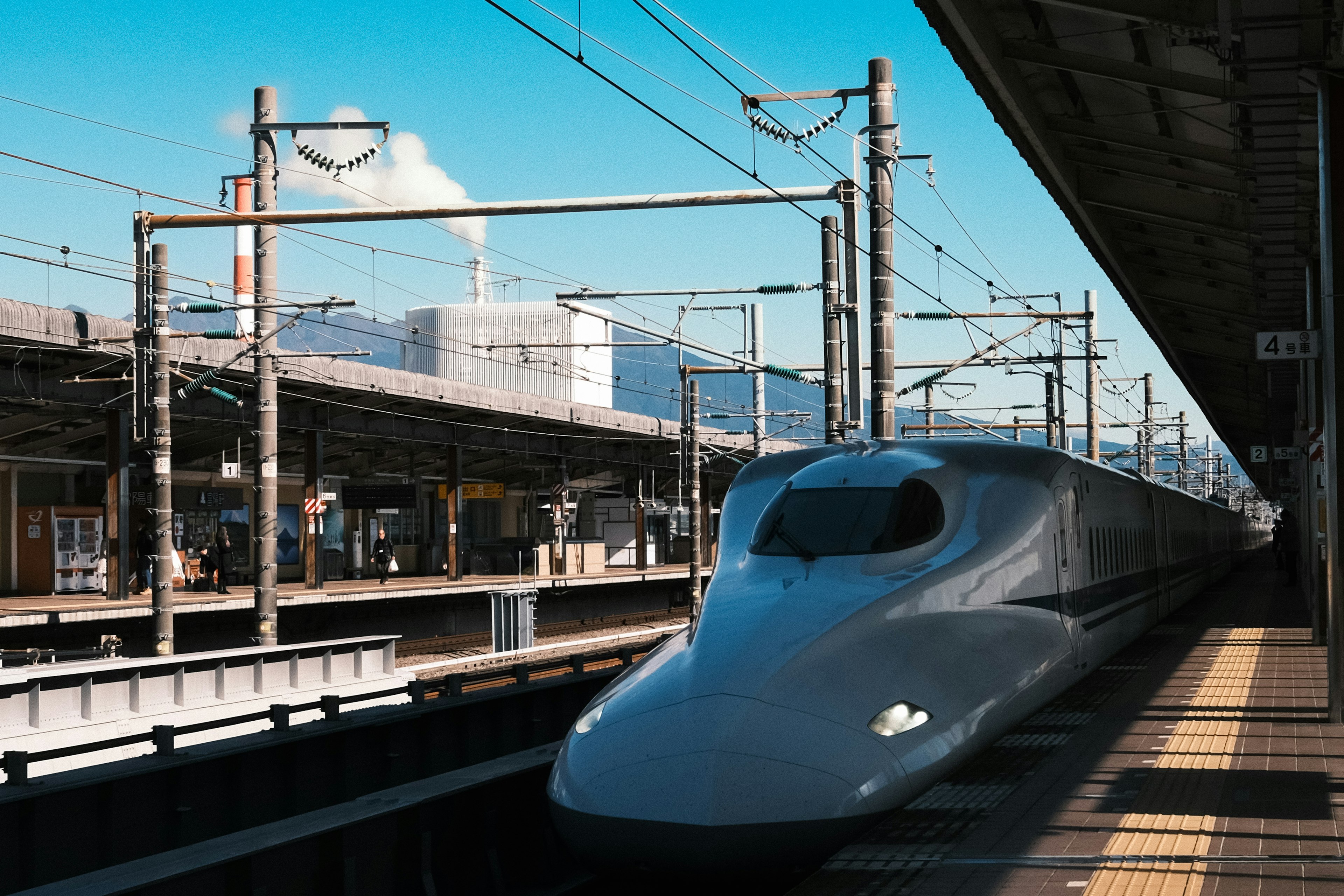 Kereta Shinkansen di stasiun dengan langit biru dan cerobong pabrik di latar belakang