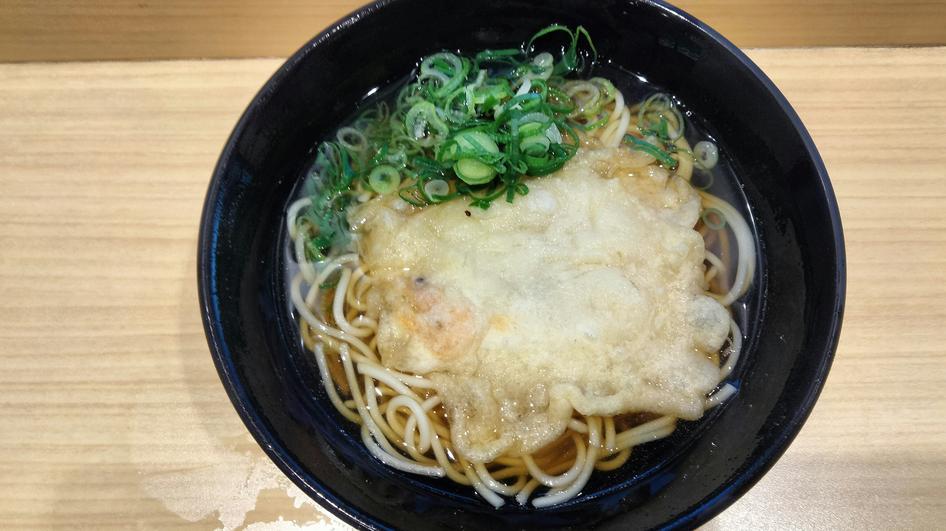 bowl of udon topped with green onions and a fried tempura