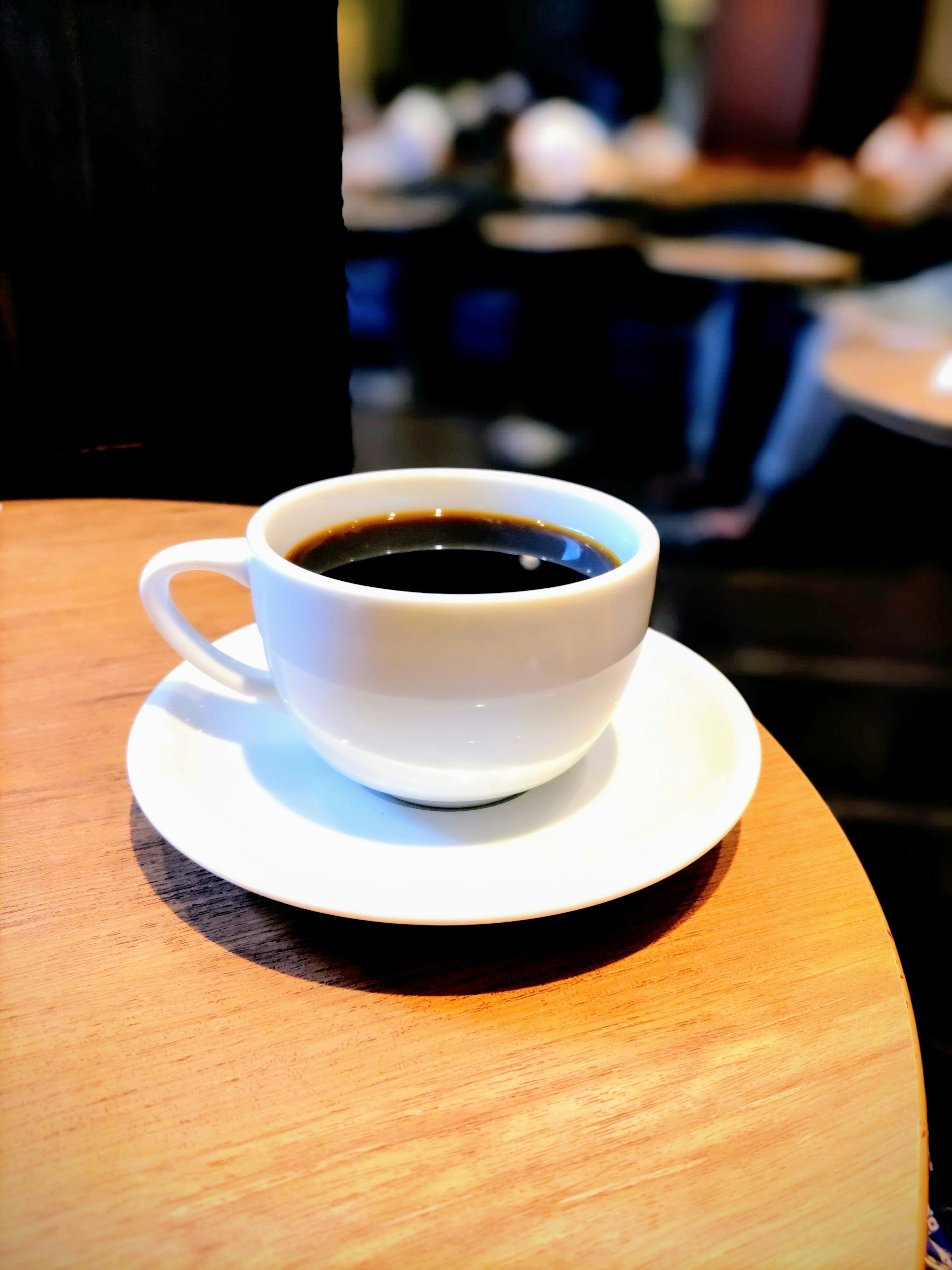 Una taza blanca de café negro sobre una mesa de madera