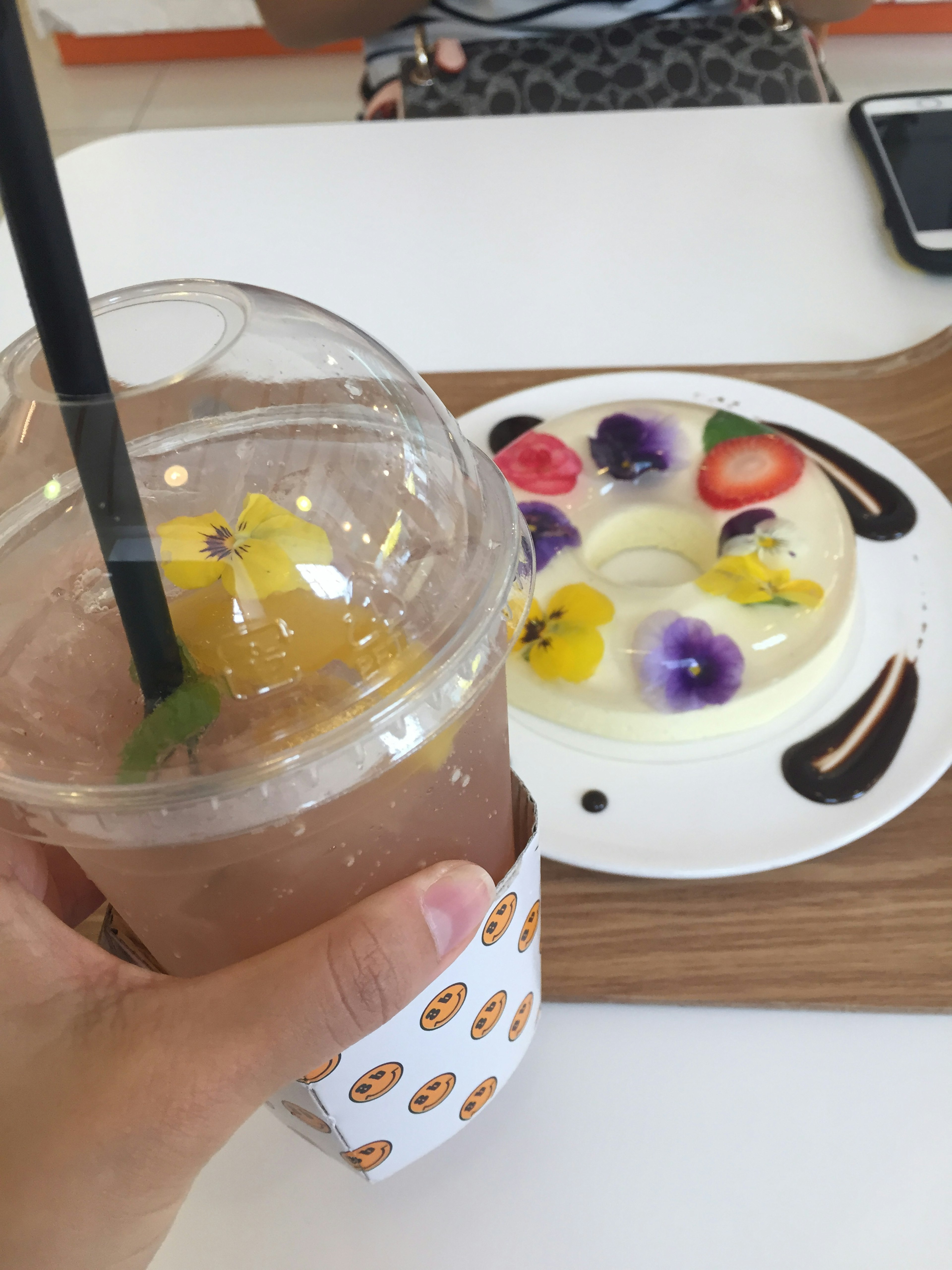 A hand holding a drink with a floral dessert on a table