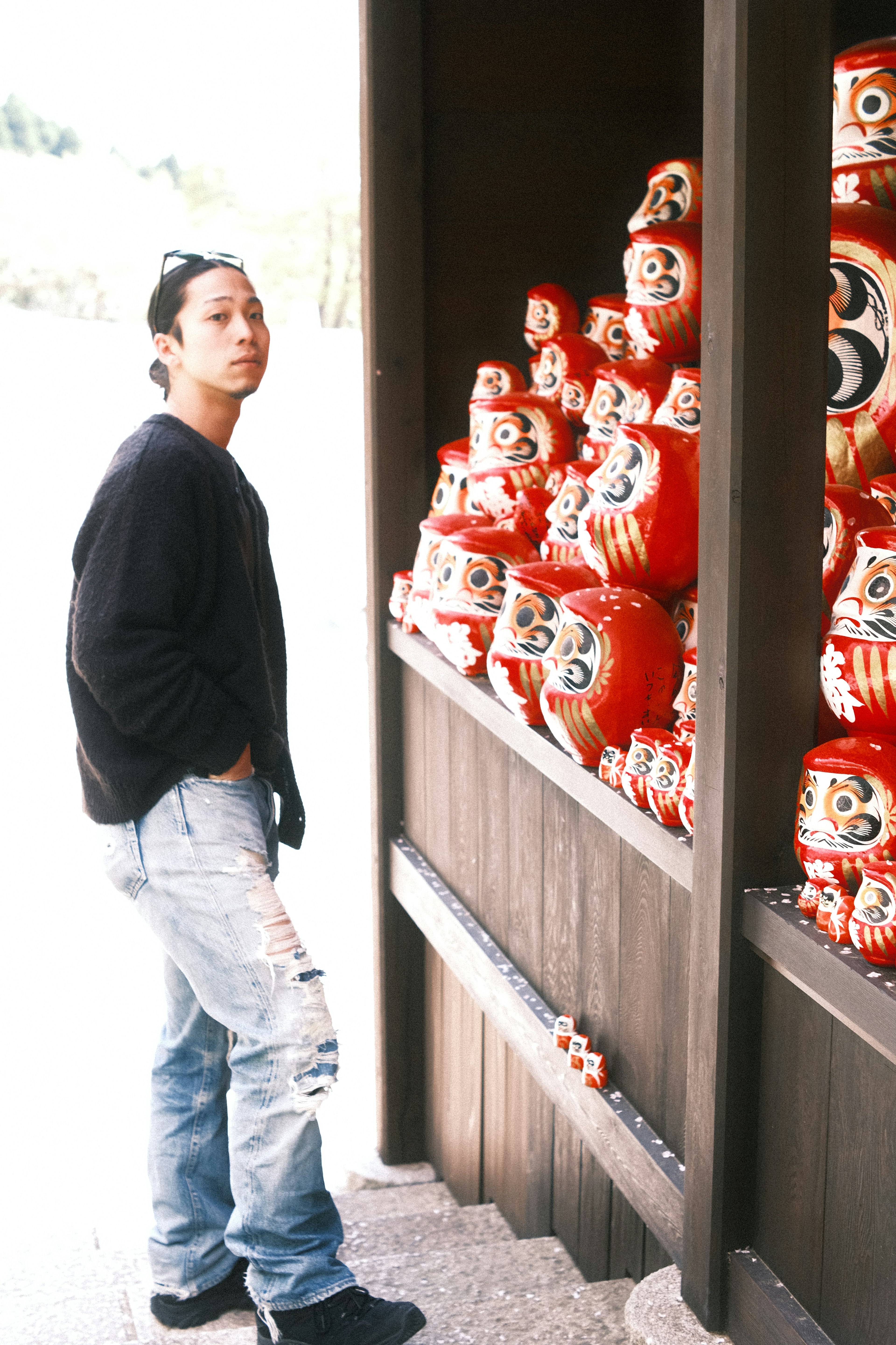 Young man standing in front of a display of red Daruma dolls and traditional culture