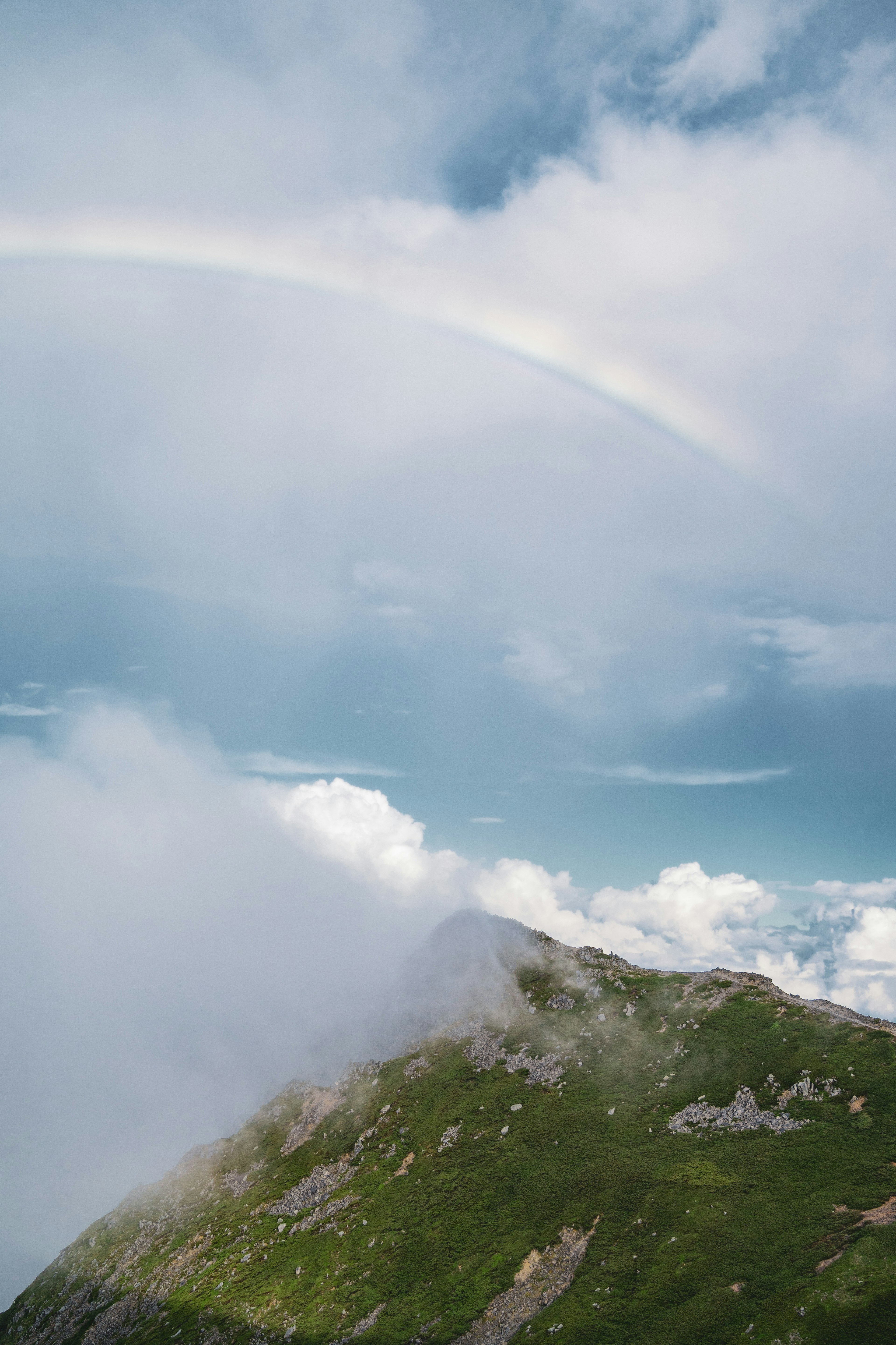 A rainbow arching over a mountain covered in clouds and blue sky