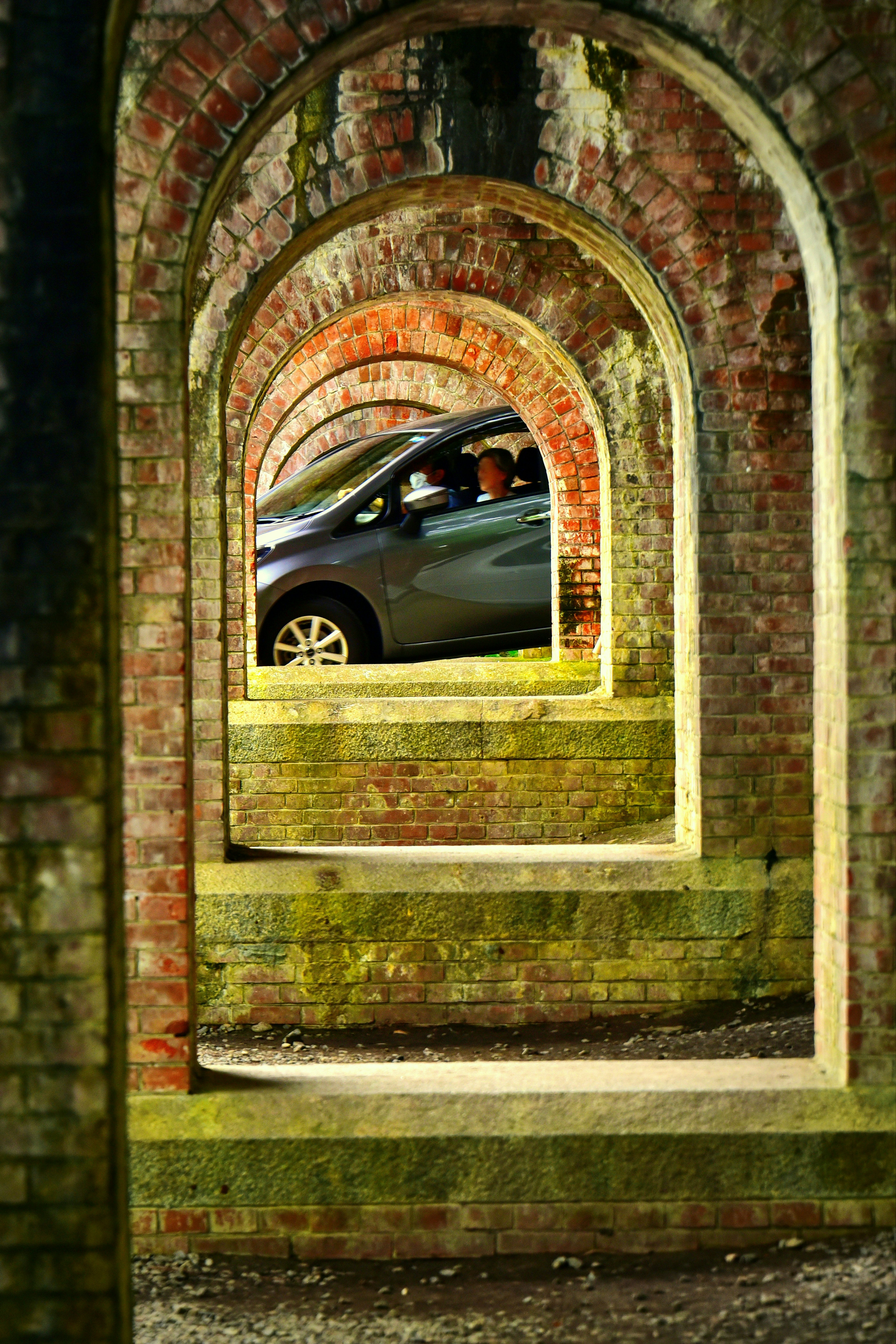 Gray car visible through a series of arched brick structures