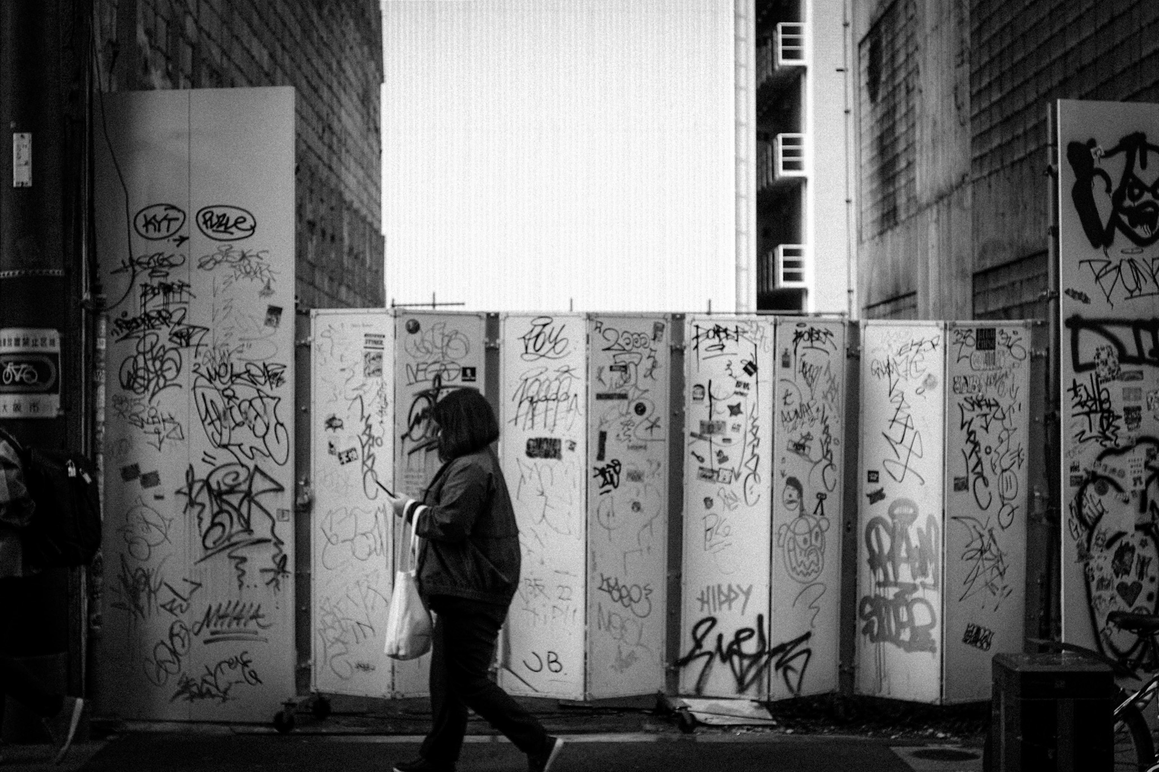 Black and white photo of a person walking in front of graffiti-covered walls