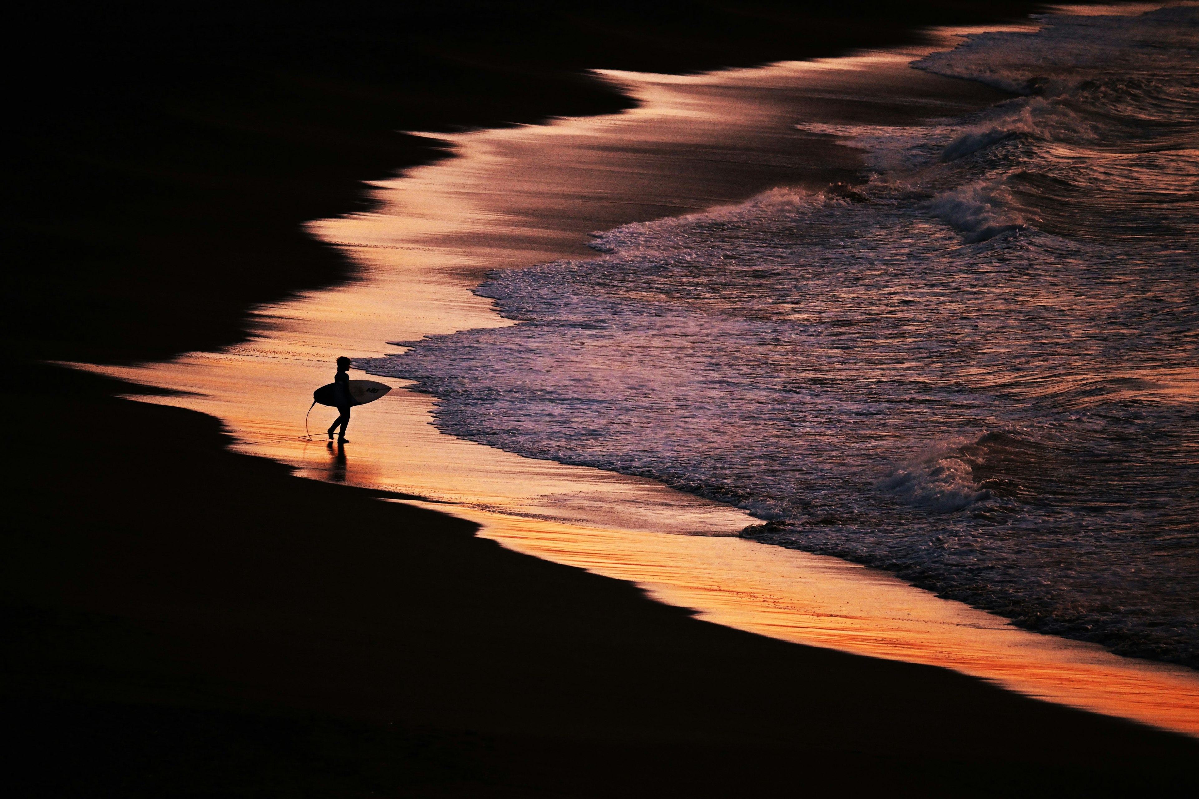 Silhouette di un surfista che cammina lungo la spiaggia al tramonto