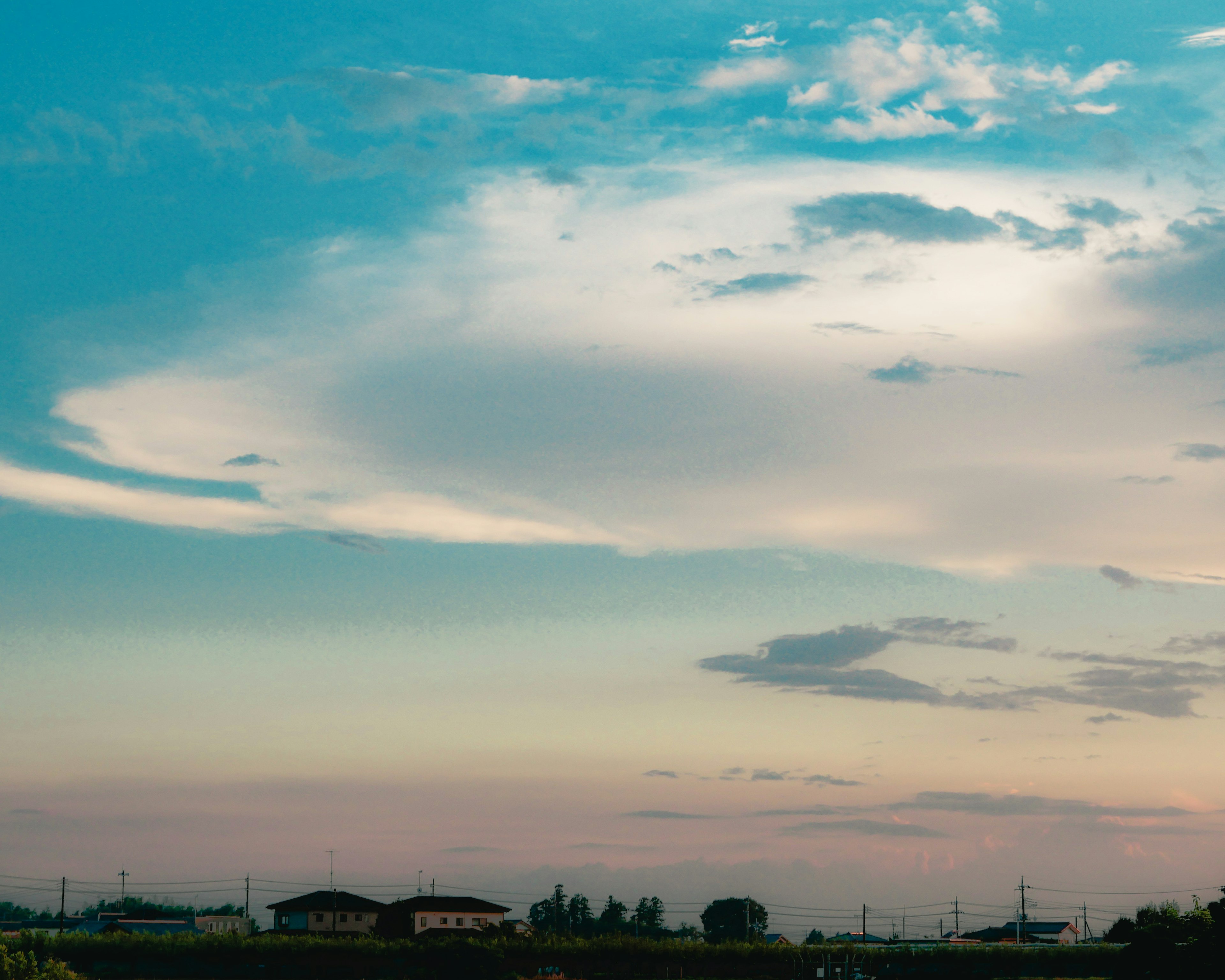 Cielo de atardecer vibrante con nubes expansivas y siluetas de casas