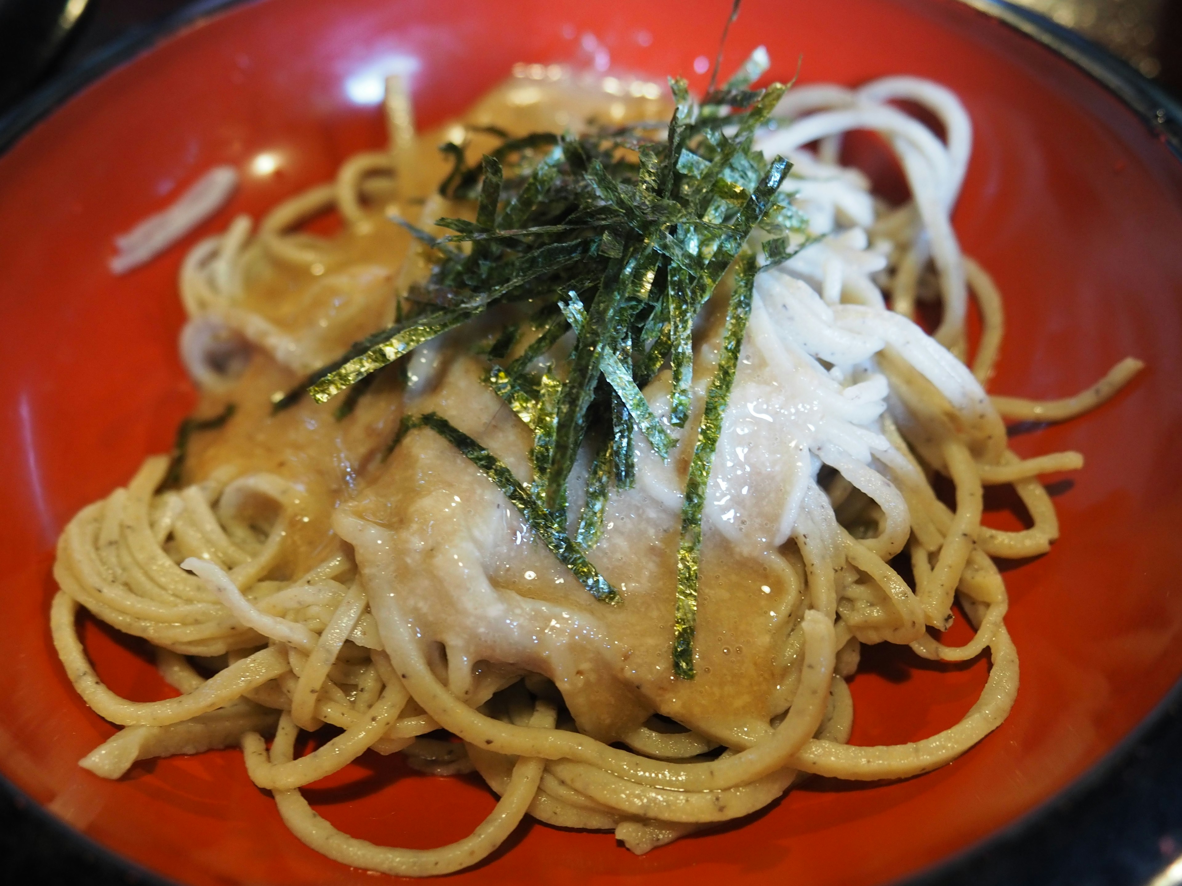 Fideos finos servidos en un tazón rojo cubiertos con alga