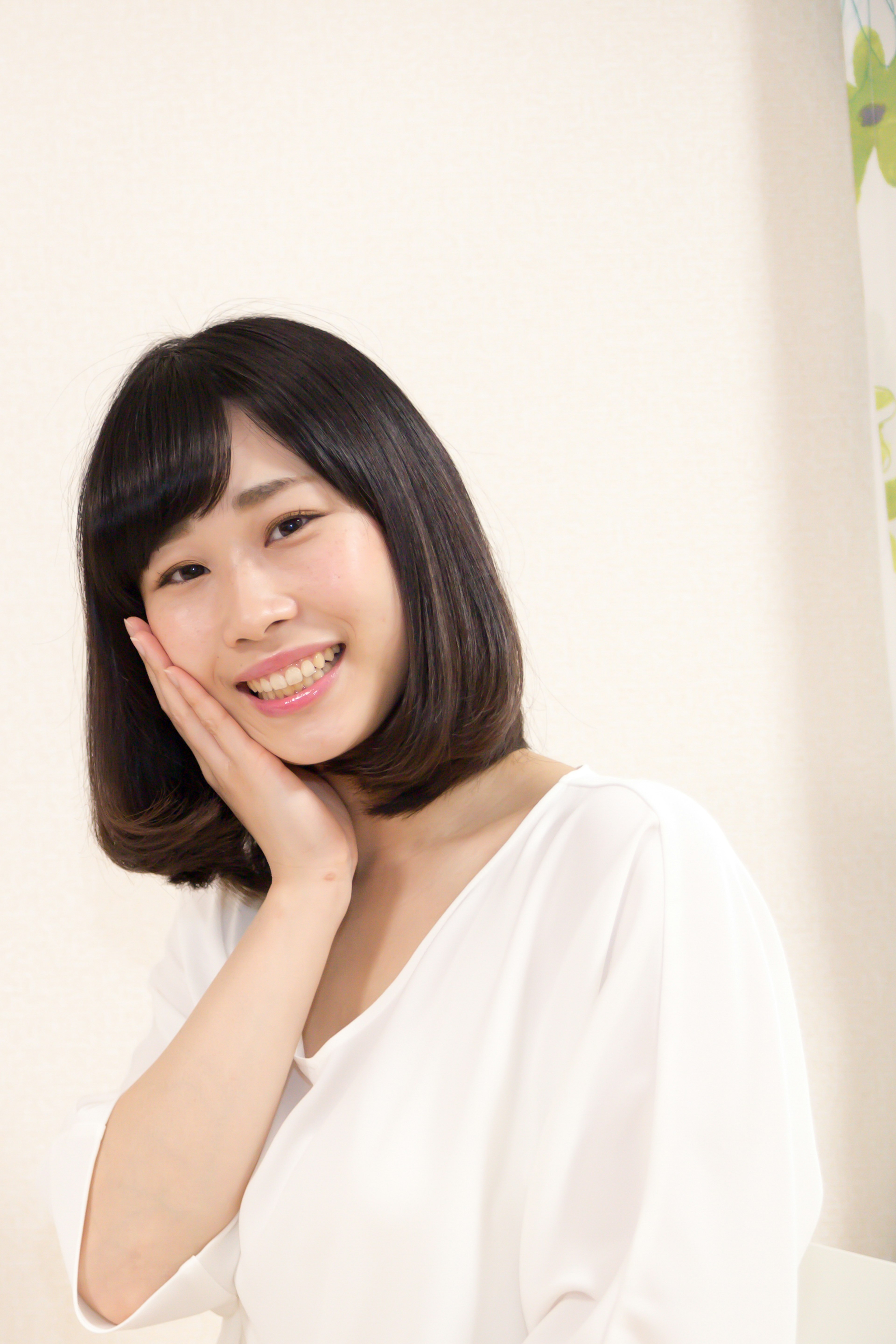 A smiling woman in a white blouse resting her hand on her cheek