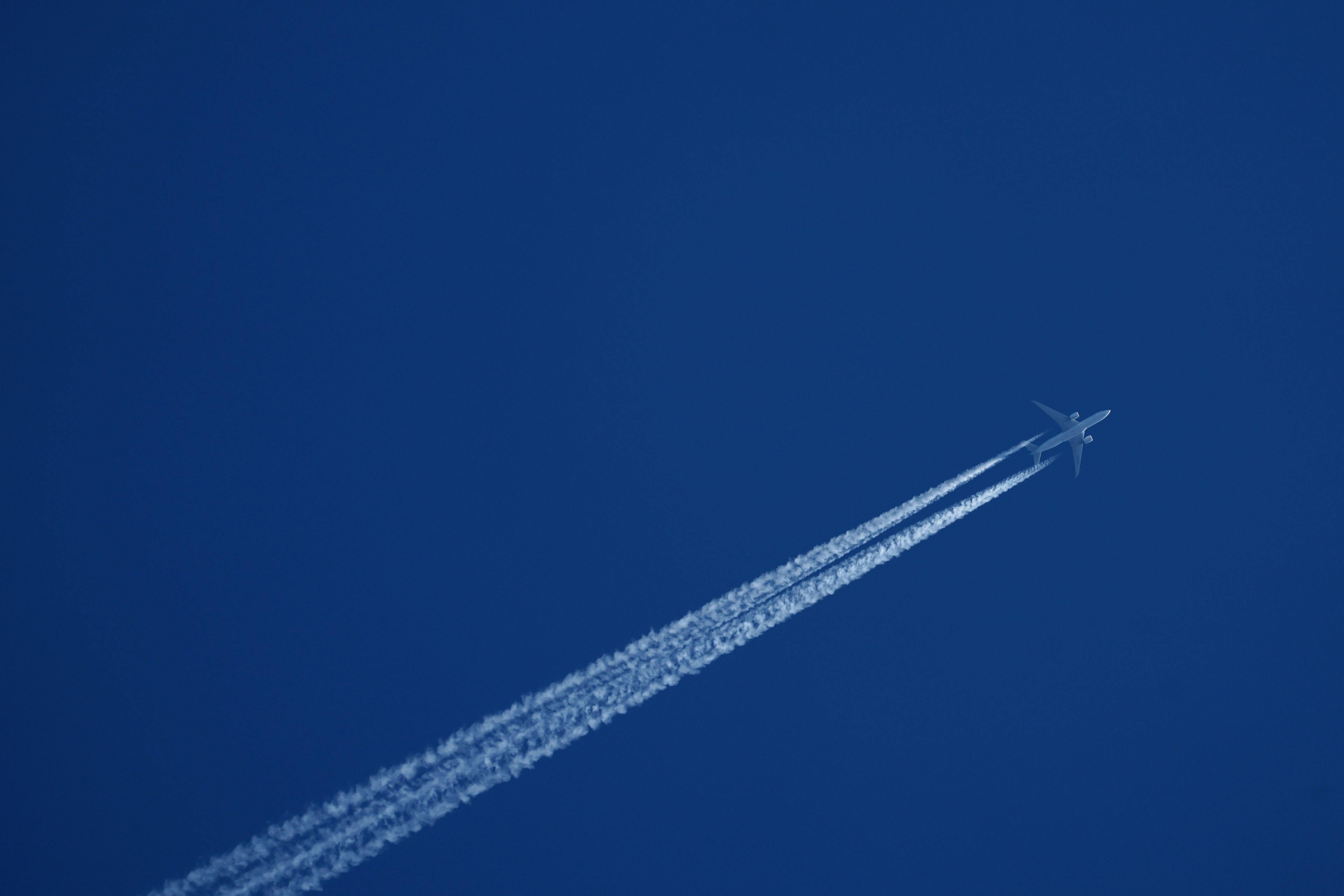 Un aereo che vola in un cielo blu chiaro con una scia bianca