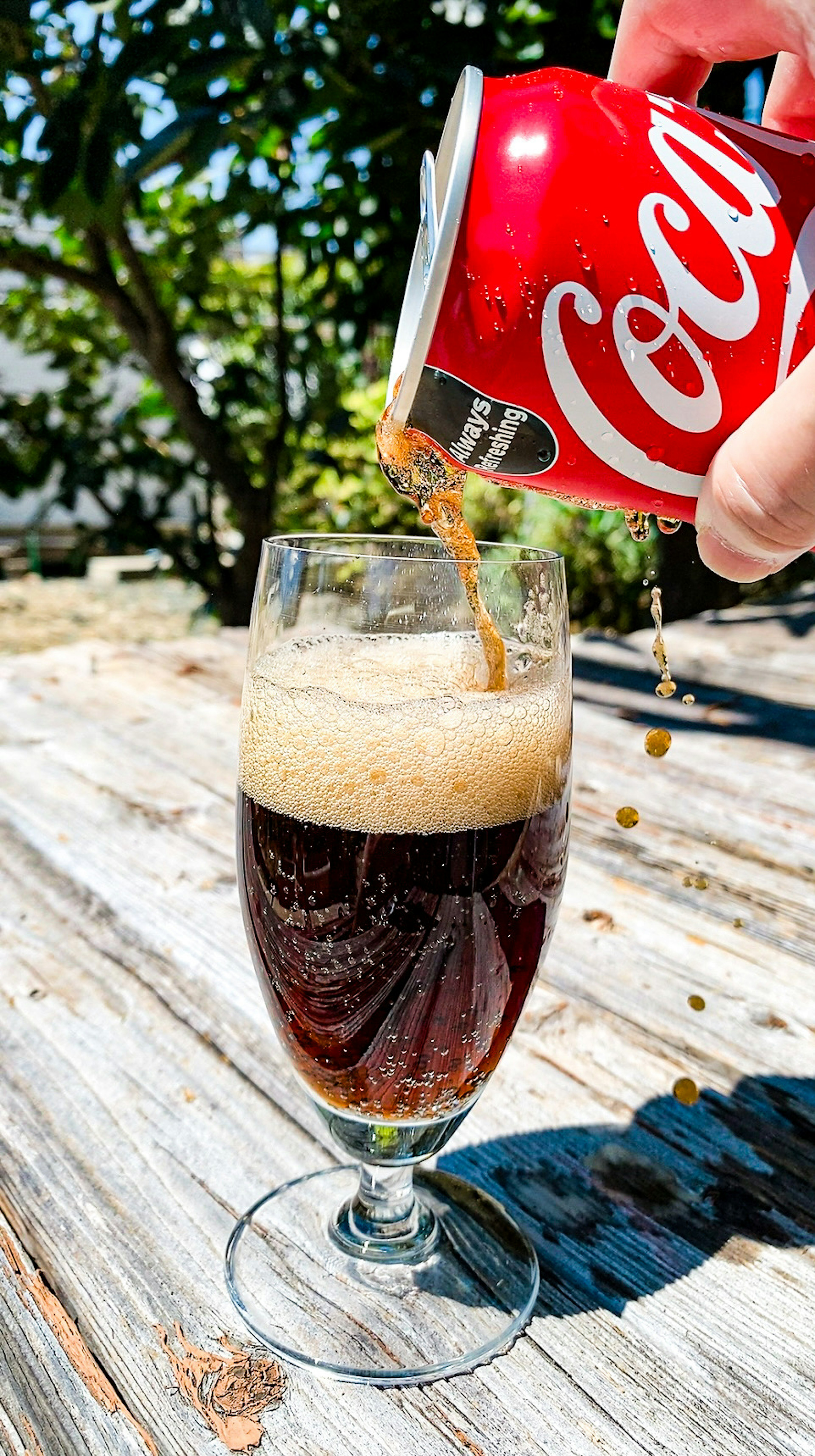 Cola aus einer roten Coca-Cola-Dose in ein Glas mit Schaum gießen