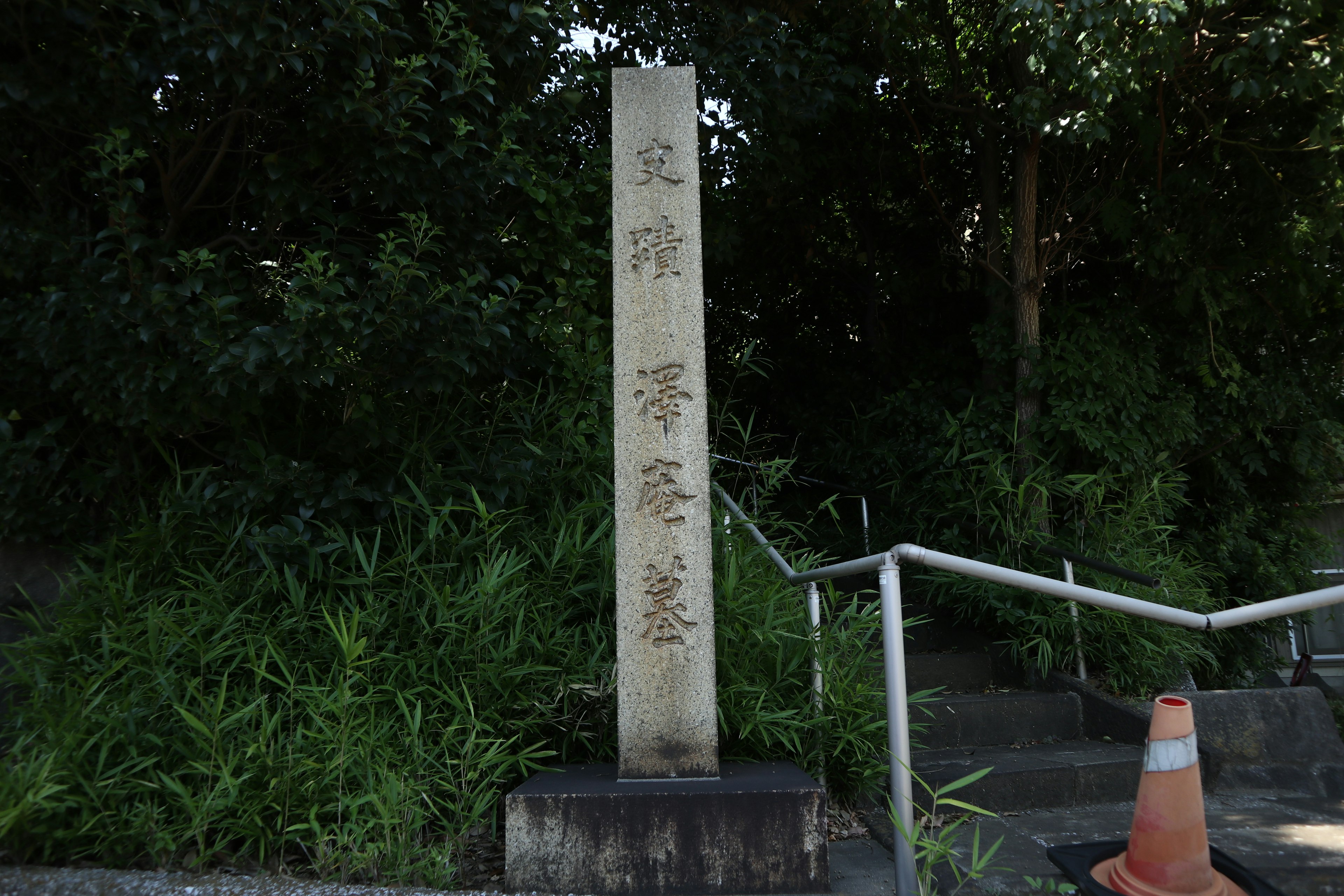 Stone marker with inscriptions beside a staircase and lush greenery in the background