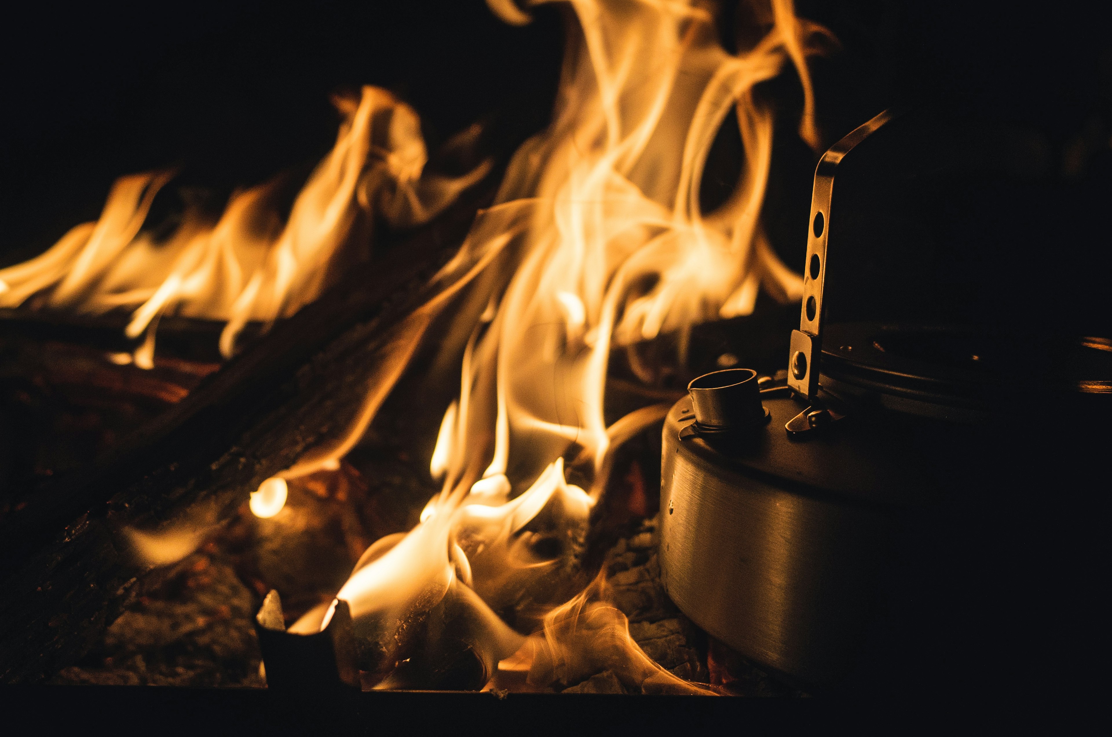 Flames of a campfire with a metal cooking device nearby