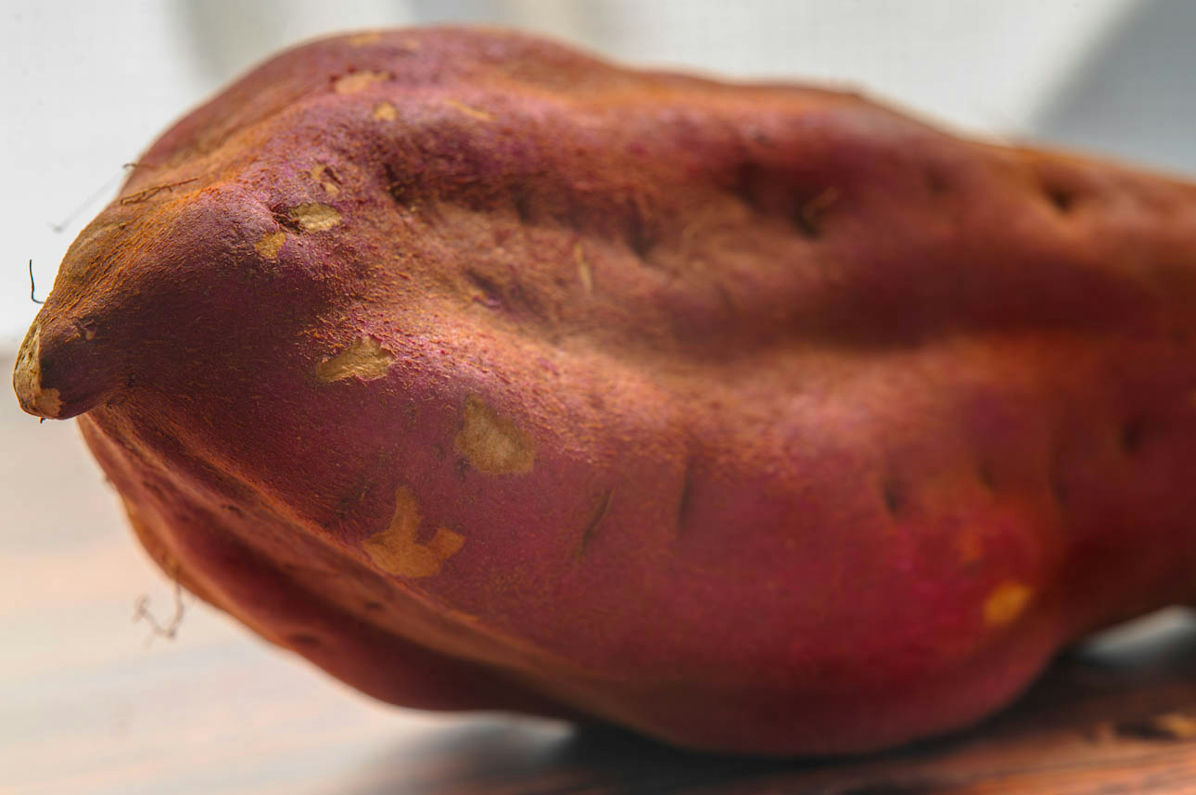 A reddish-purple sweet potato resting on a wooden table