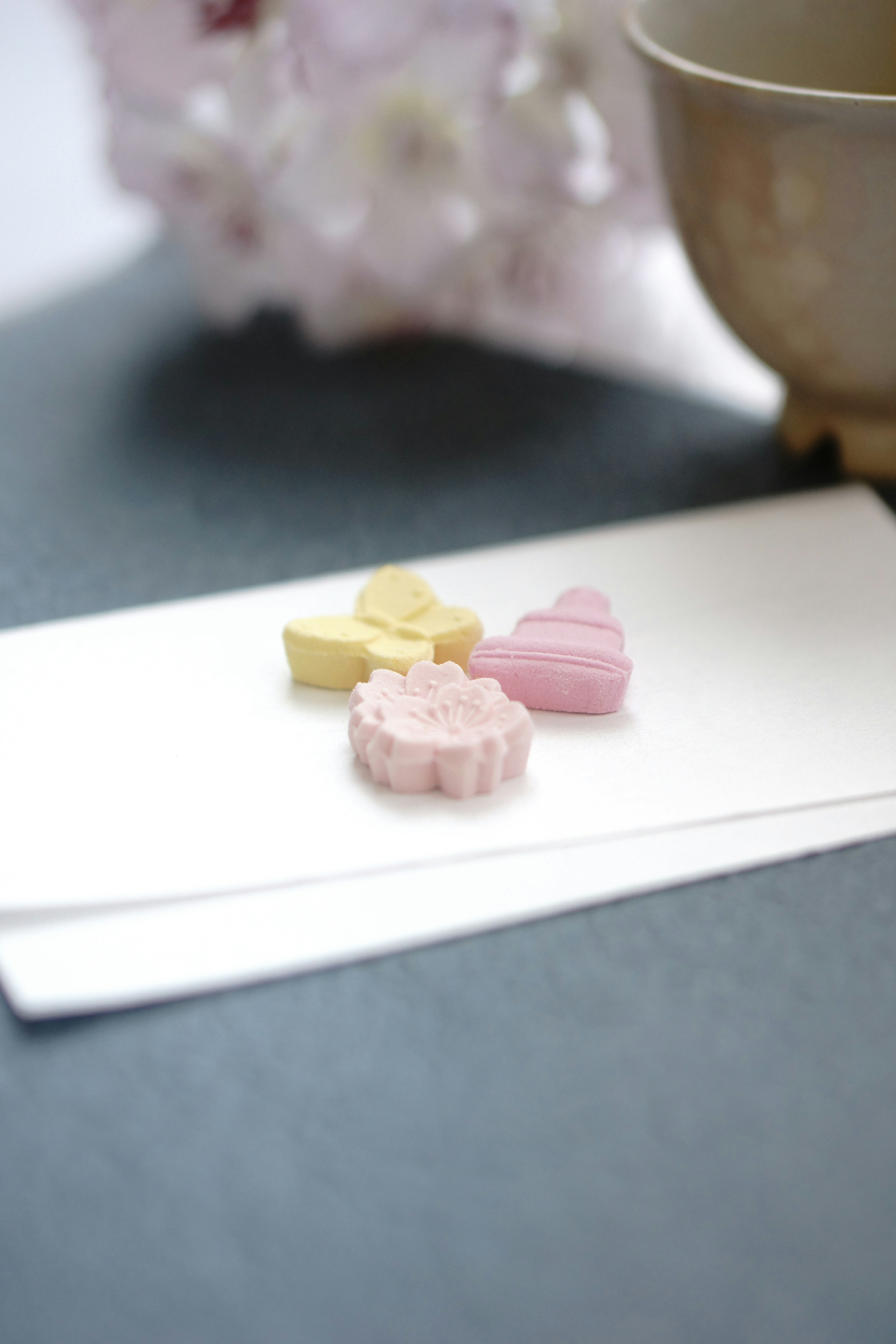 Pink and yellow heart-shaped candies on a white envelope with a brown teacup in the background