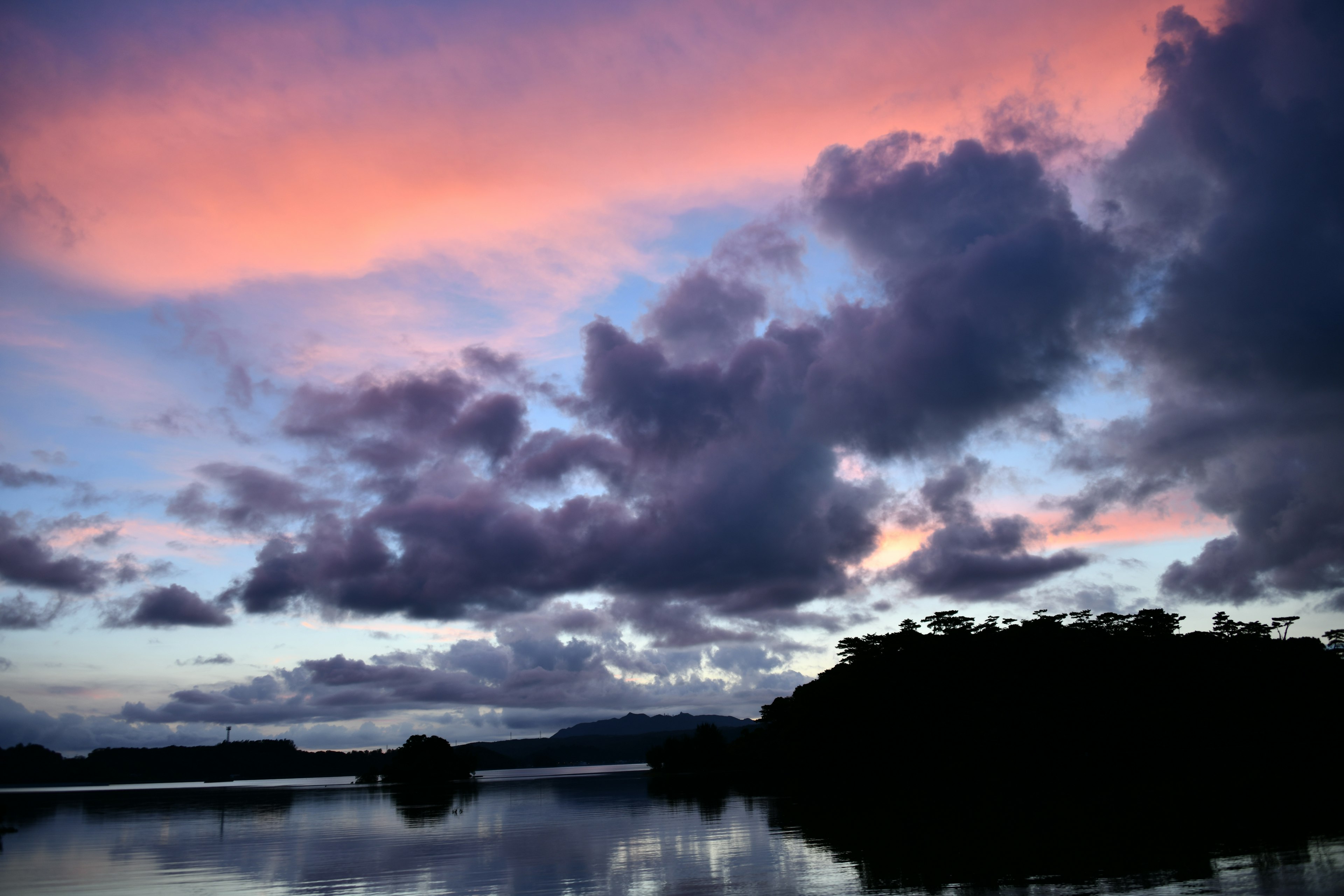 Schöner Sonnenuntergangshimmel über einem See mit dunklen Baumsilhouetten, die sich im Wasser spiegeln