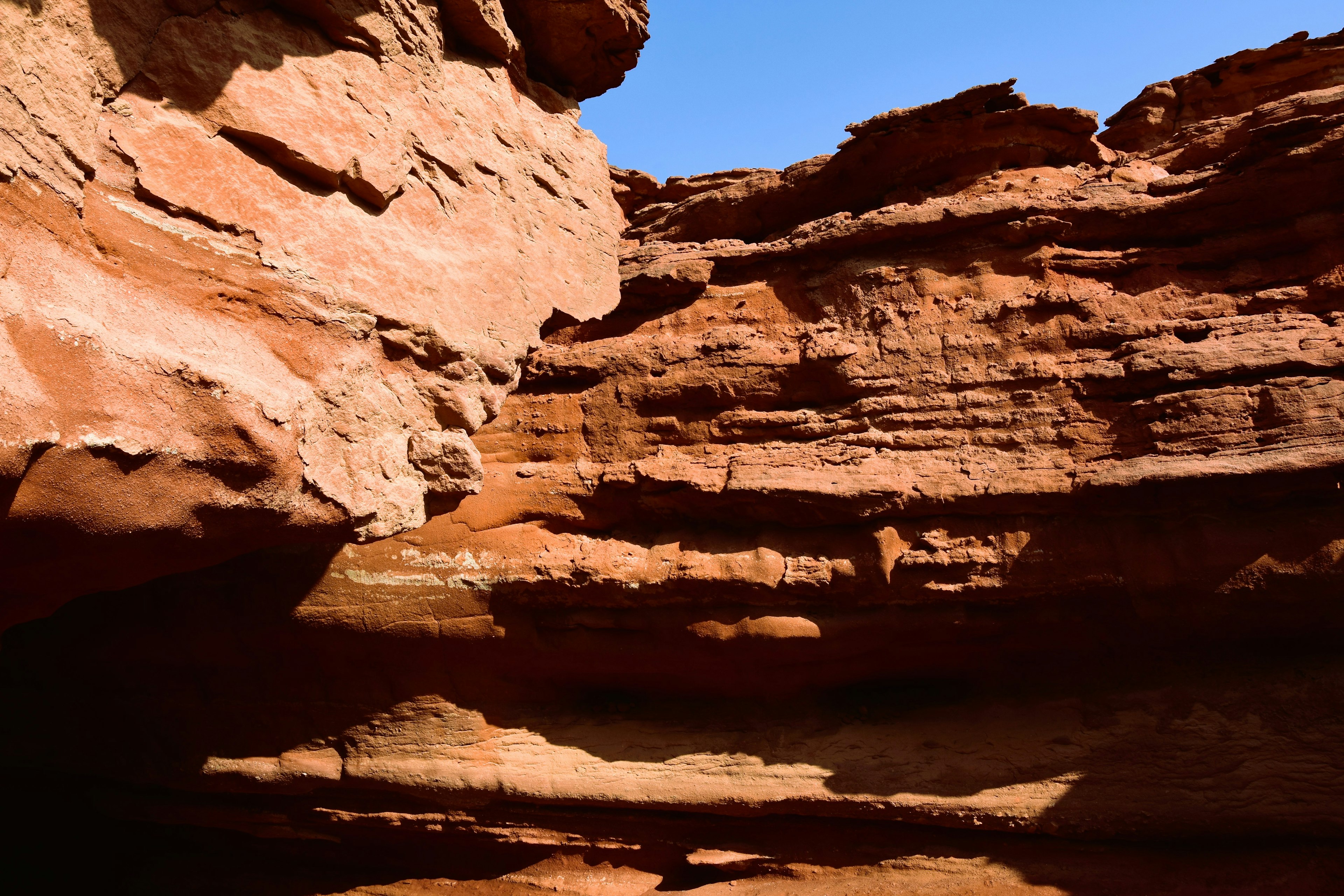 Vista di un canyon con formazioni rocciose rosse stratificate e un cielo blu chiaro