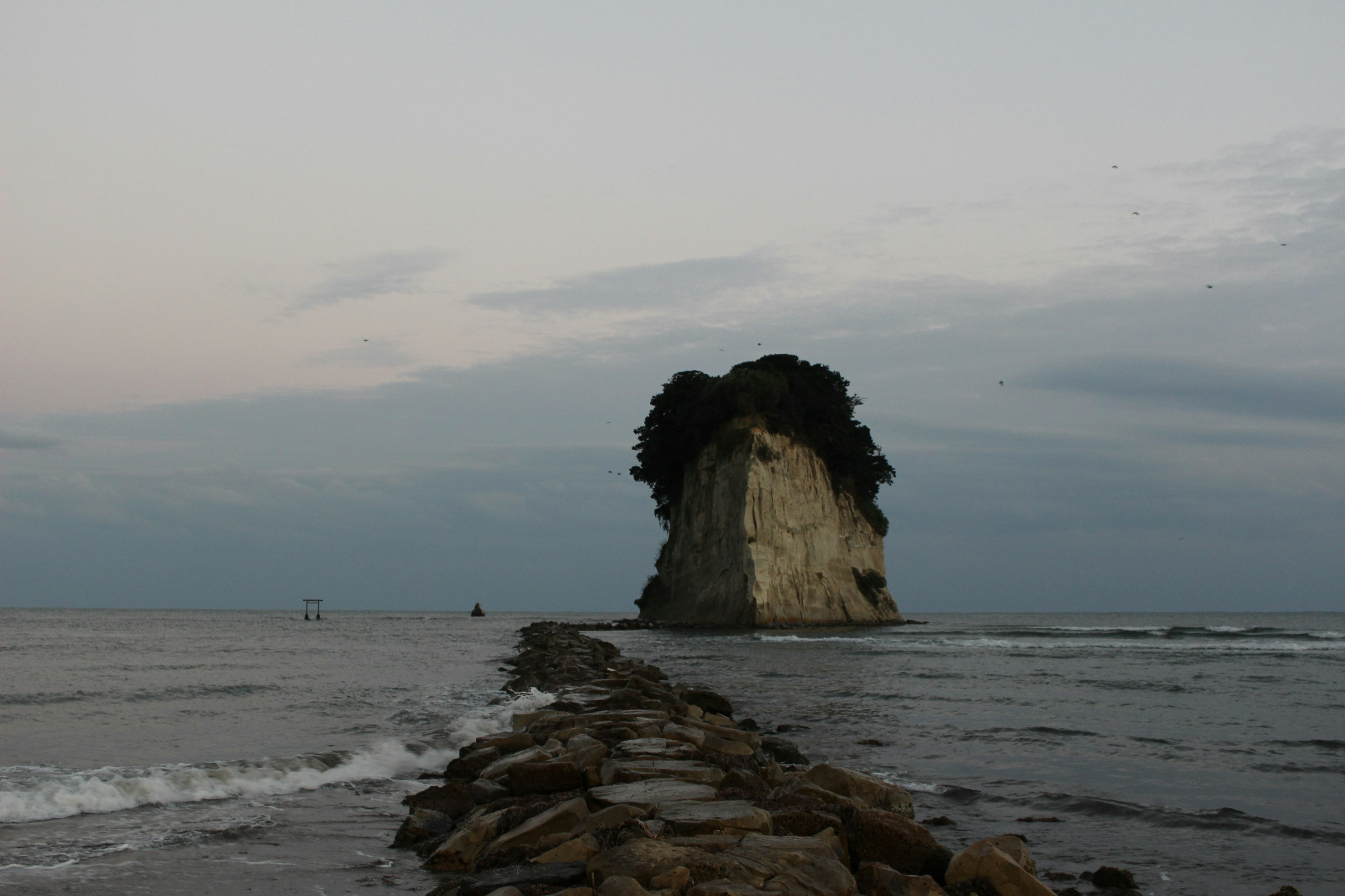 Großer Felsen umgeben von Wasser mit einem Steinpier, der zu ihm führt