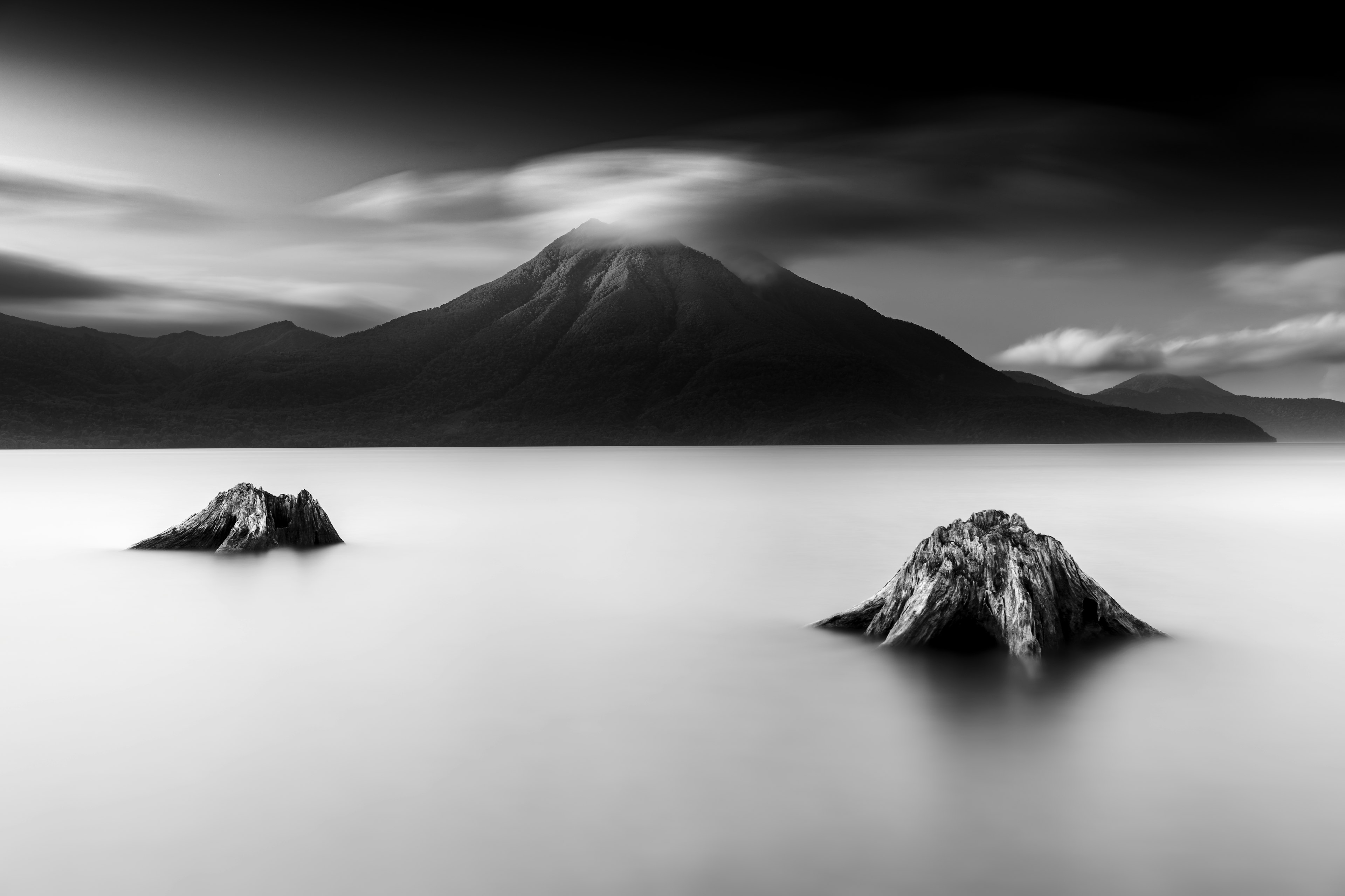 Gambar monokrom danau tenang dengan batu dan gunung di latar belakang