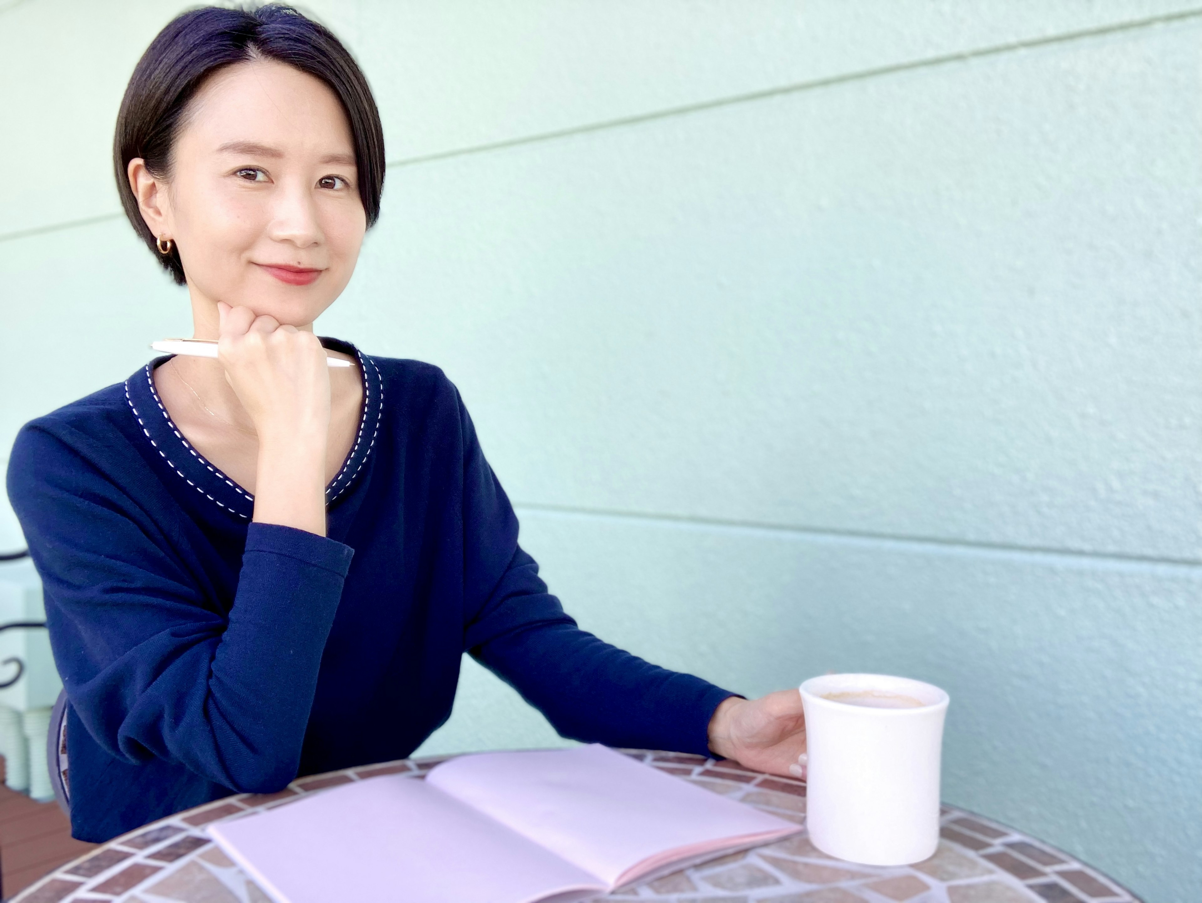 Eine Frau in einem blauen Pullover sitzt an einem Café-Tisch und hält eine Tasse Kaffee