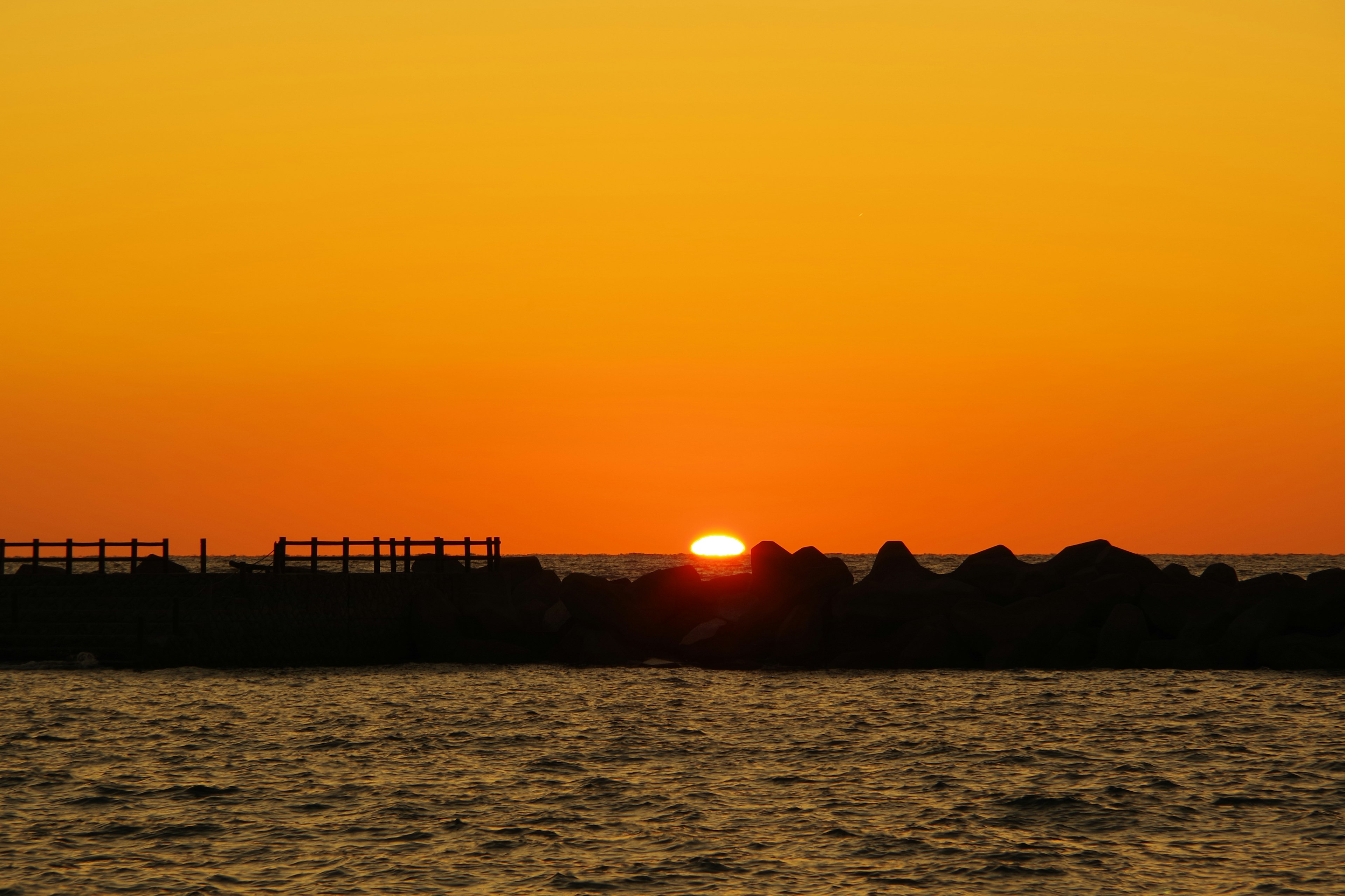 Sonnenuntergang über dem Ozean mit einem lebhaften orangefarbenen Himmel und dunklen Felsen-Silhouetten